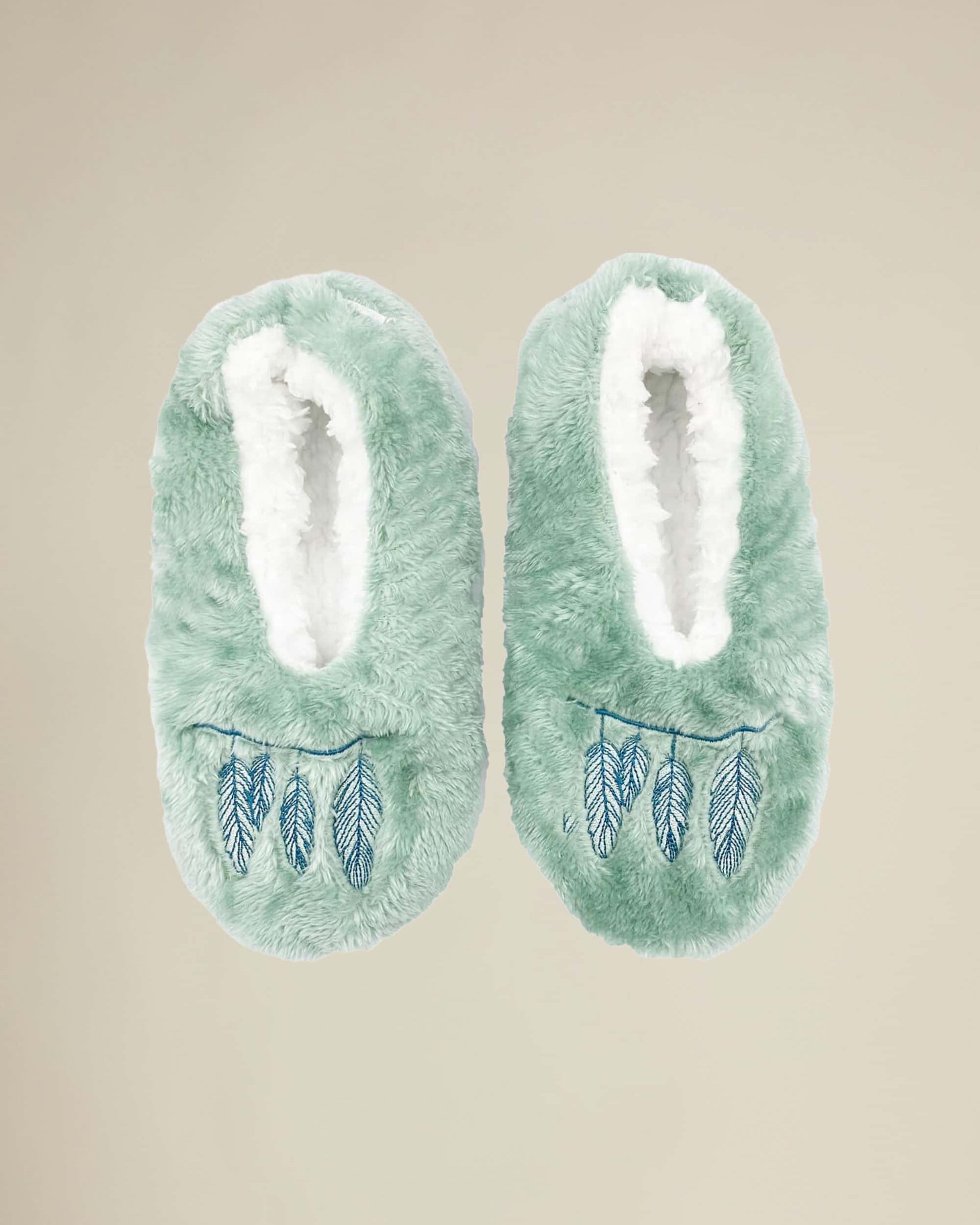A pair of green plush slippers with a dreamcatcher-inspired design on the top.