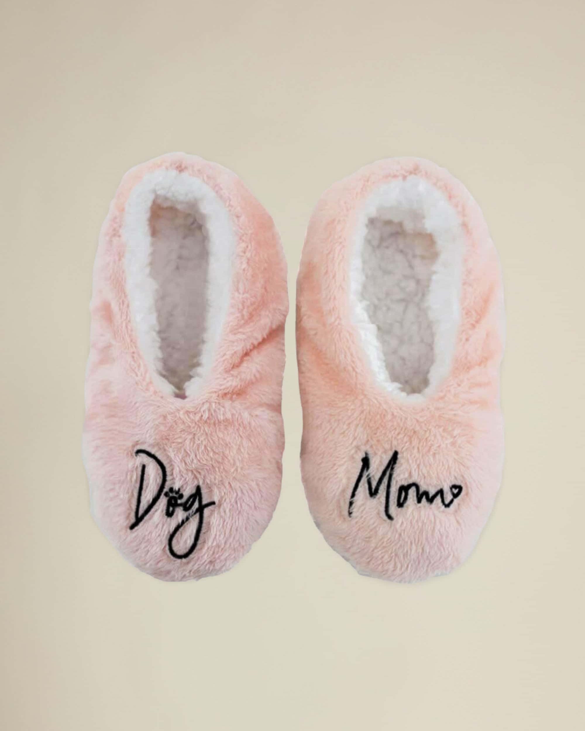 A pair of pink slippers with 'Dog Mom' written on the top, designed for indoor use with a plush, soft interior and skid-resistant rubber soles.