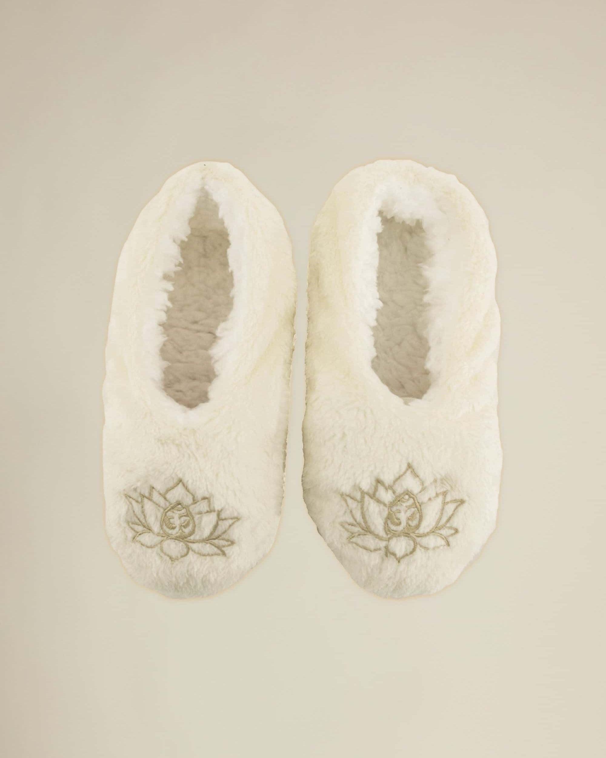 A pair of beige lotus footsies slippers with a floral design on the top, intended for indoor use.