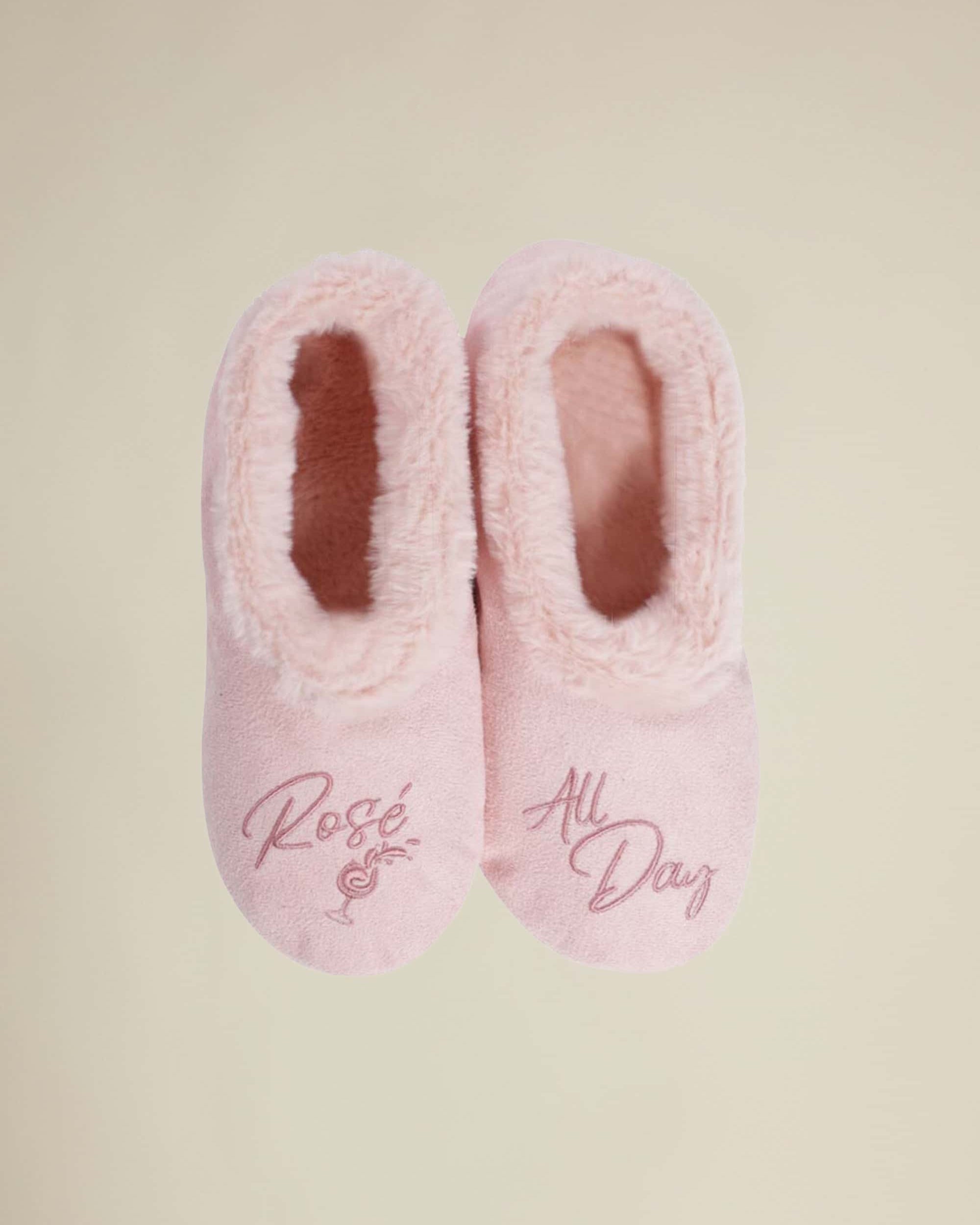 A pair of pink slippers with 'Rosé All Day' text and a plush, soft fur lining designed for indoor use.