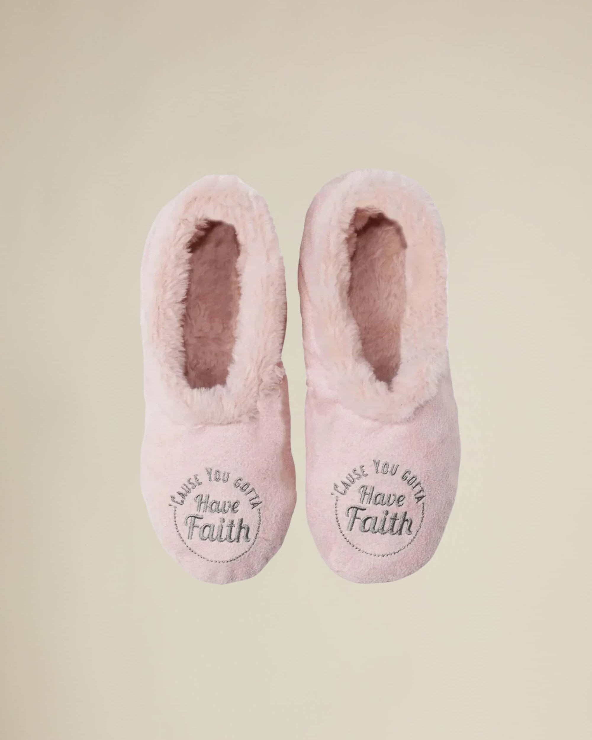A pair of pink plush slippers with 'Gotta Have Faith' text on the top, designed like socks with a stretch fit.