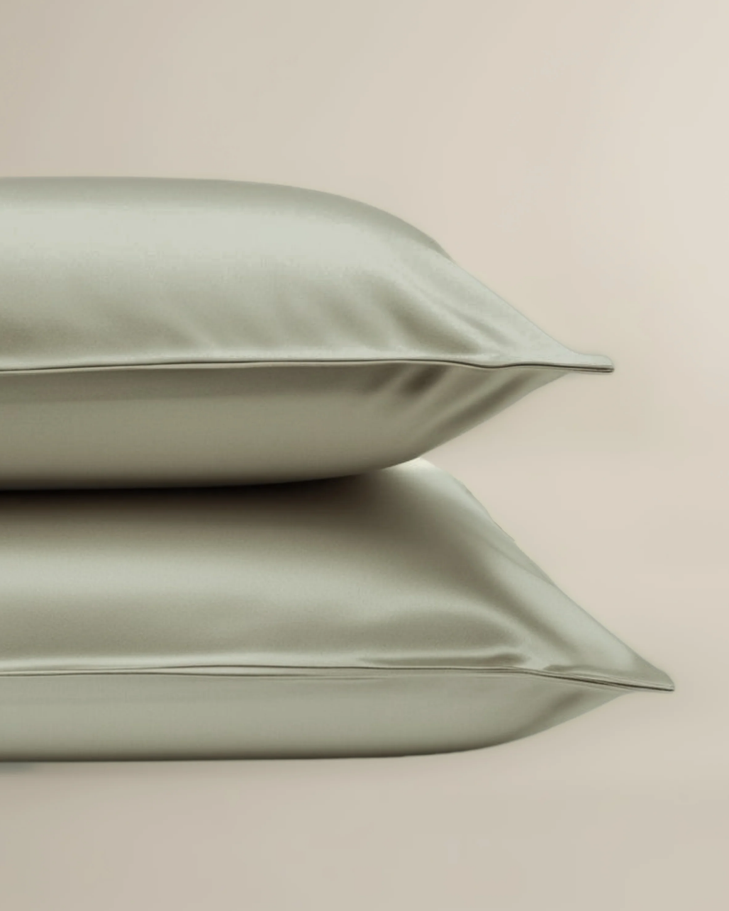 Two green satin pillows on a beige background with a certification badge in the corner.