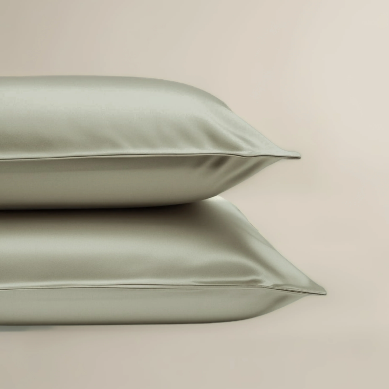 Two green satin pillows on a beige background with a certification badge in the corner.
