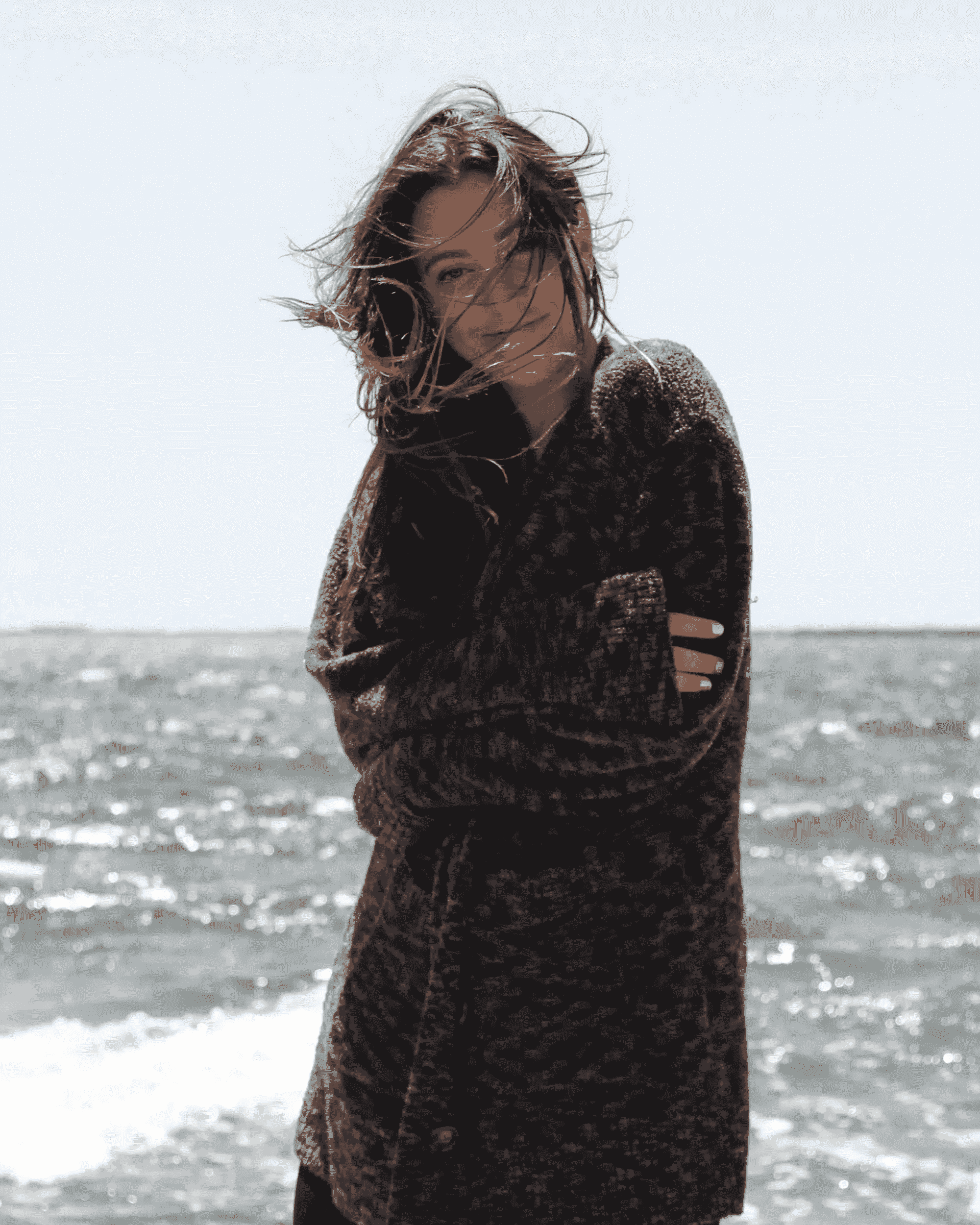 a woman stands on the beach wrapping up in a black and grey button-up cardigan