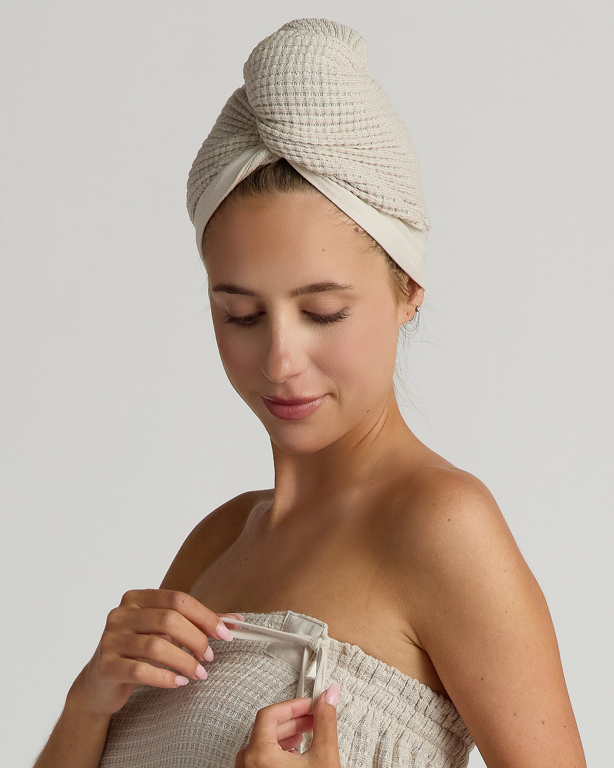 Woman wrapped in a beige spa towel with a textured hair wrap on a plain background