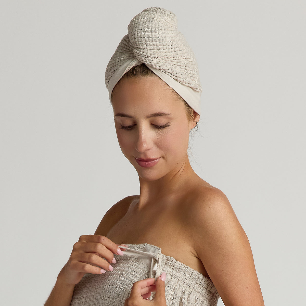 Woman wrapped in a beige spa towel with a textured hair wrap on a plain background