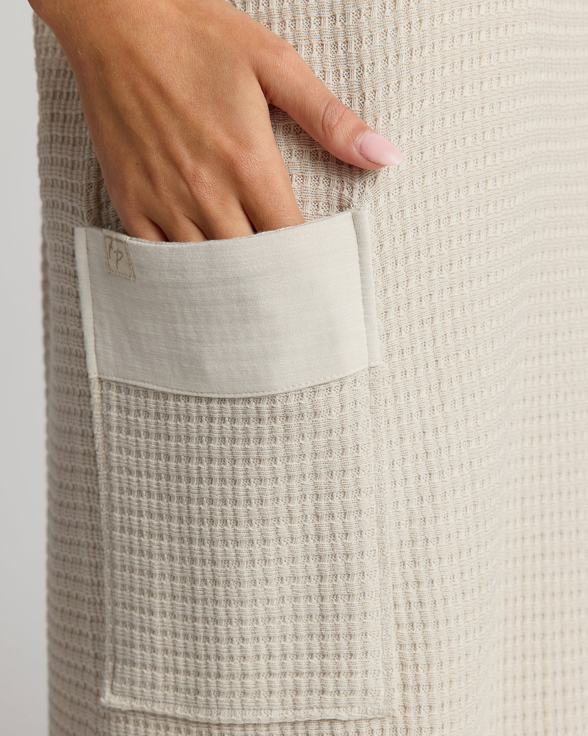 Beige waffle textured fabric with a pocket and a hand reaching into it on a light gray background