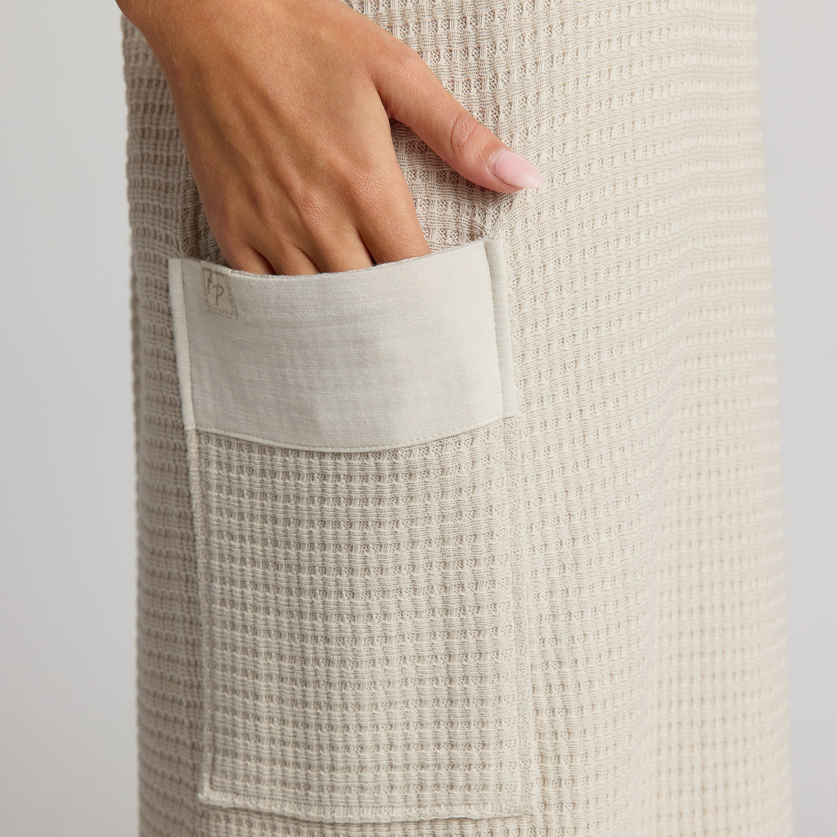 Beige waffle textured fabric with a pocket and a hand reaching into it on a light gray background