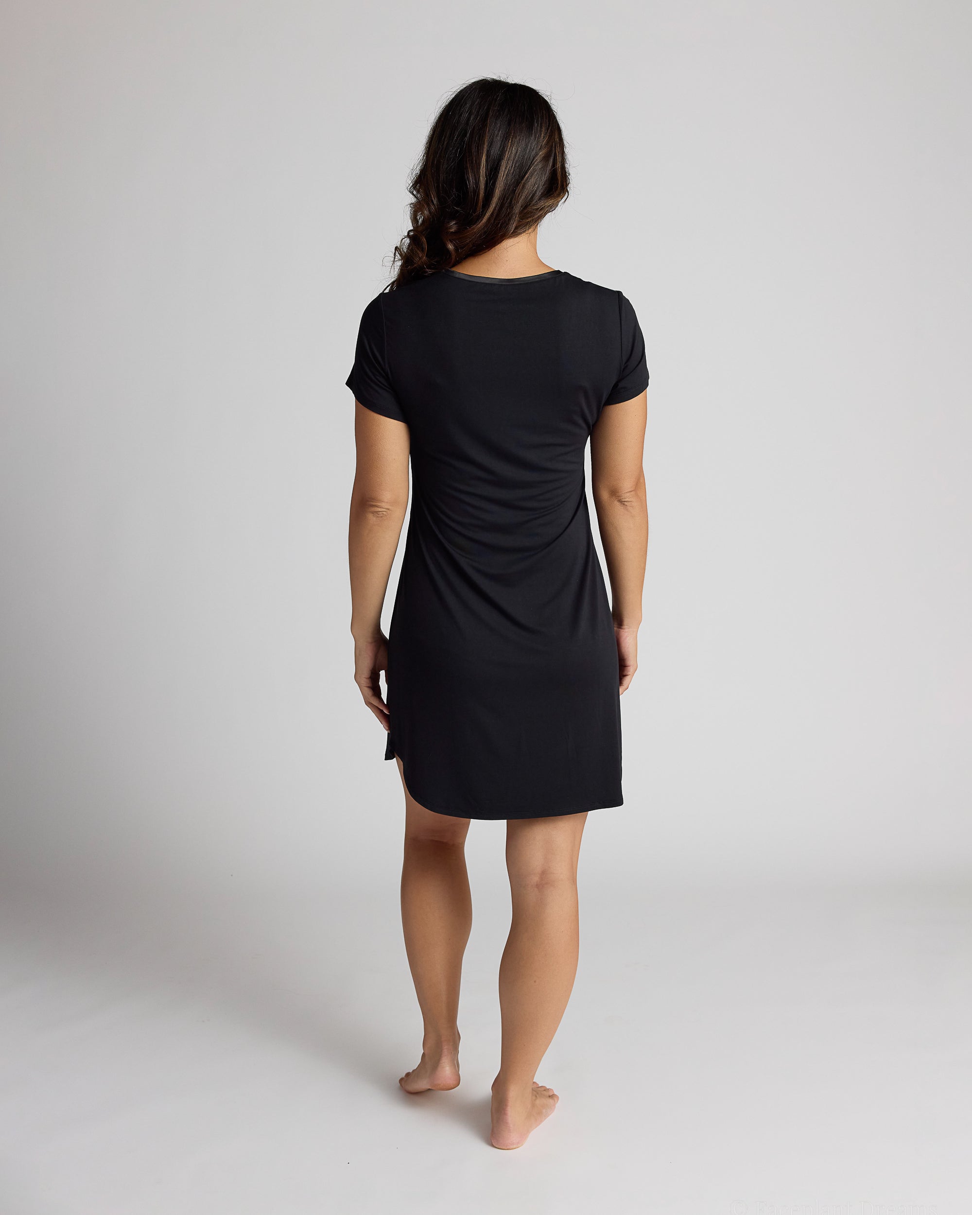 Person wearing a black dress standing against a plain background