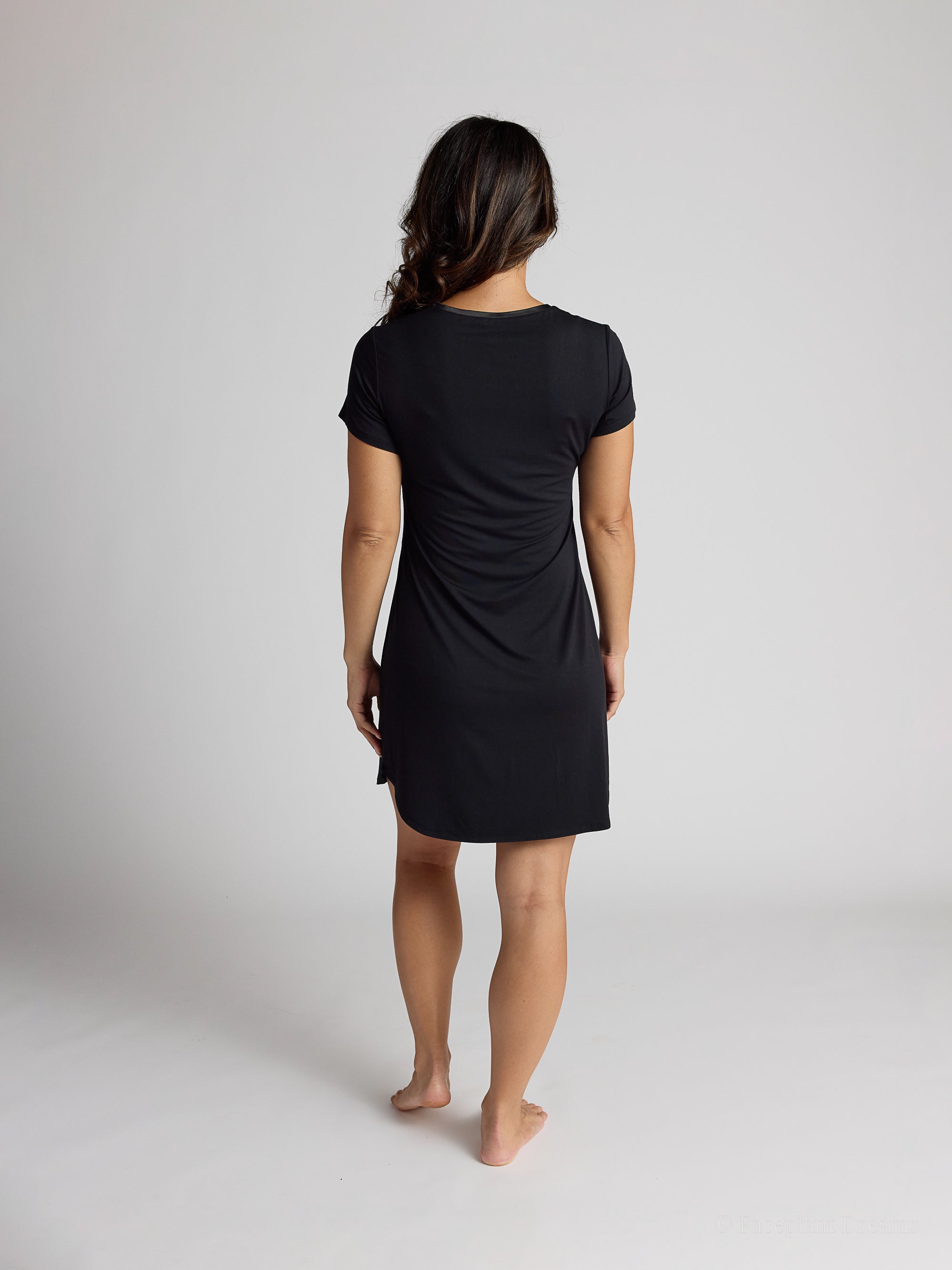 Person wearing a black dress standing against a plain background