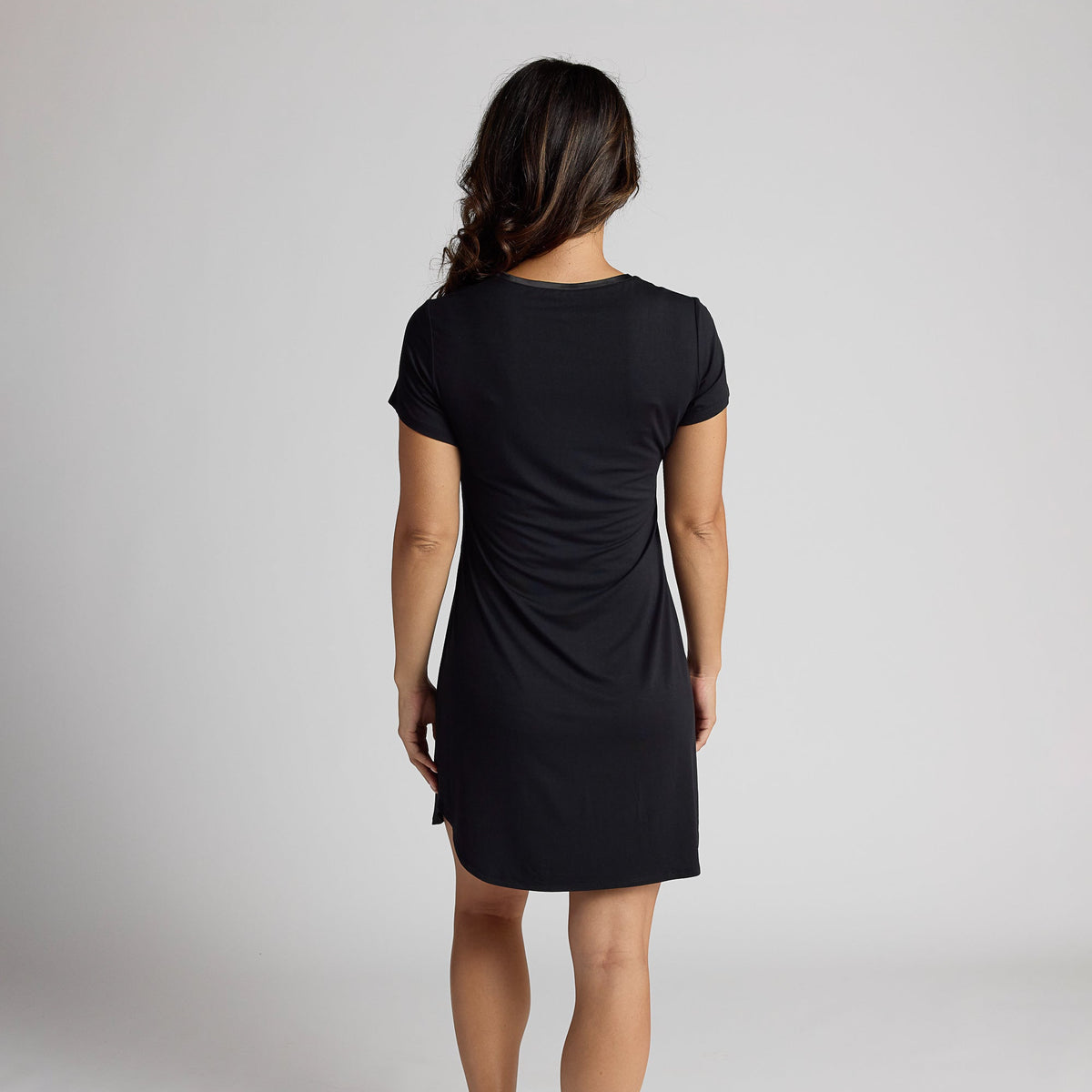 Person wearing a black dress standing against a plain background
