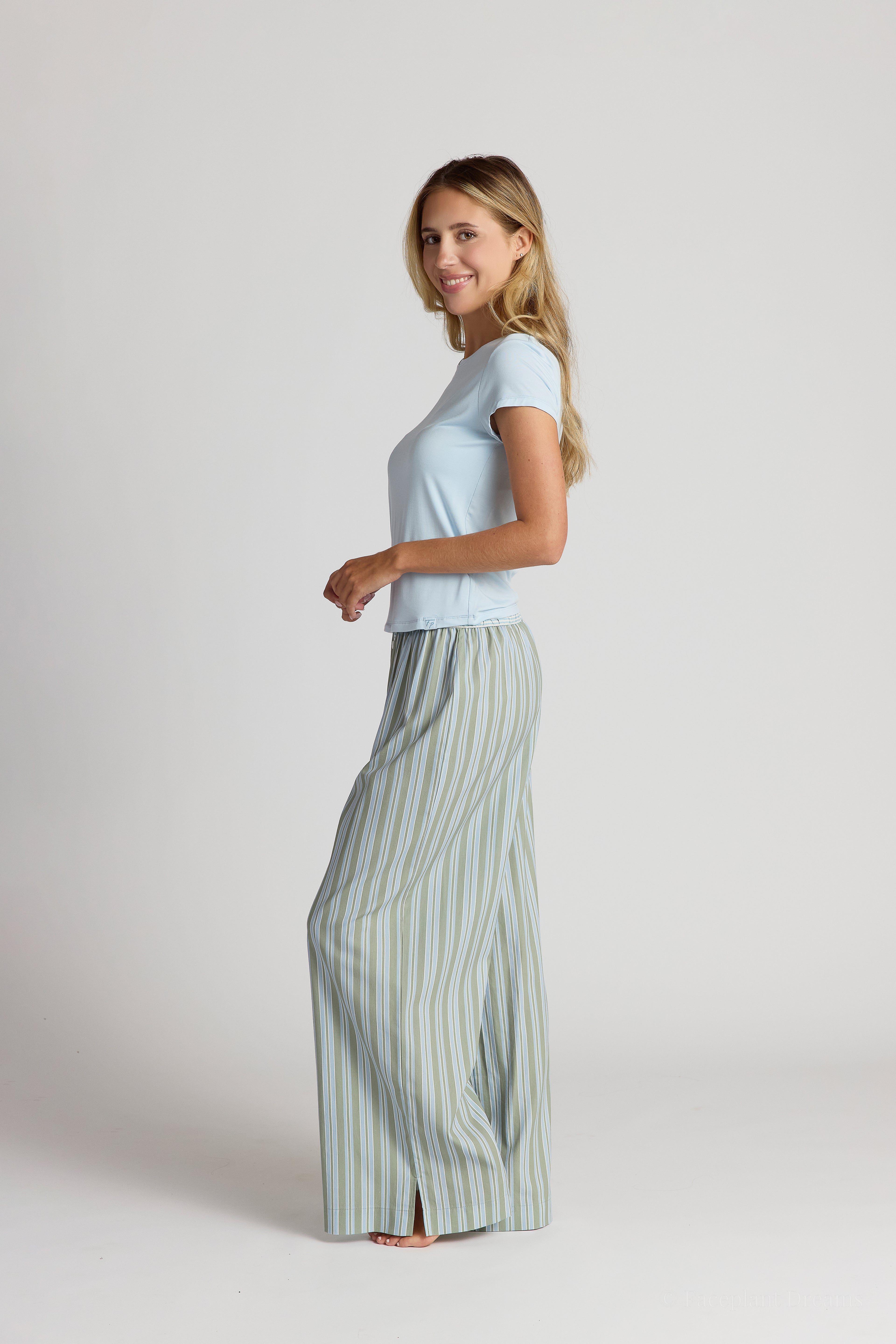 Woman wearing a light blue top and striped pajama pants on a white background
