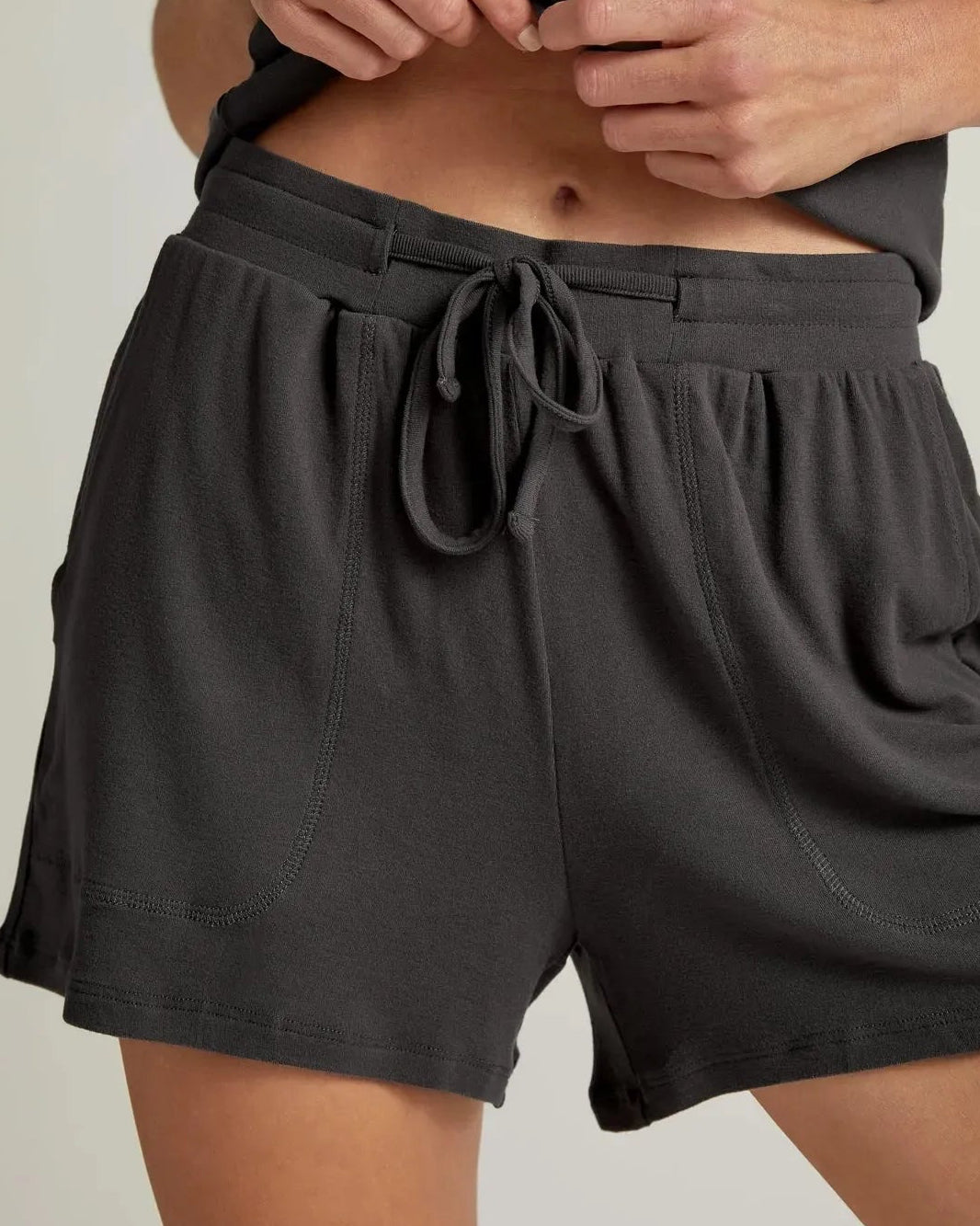 A woman wearing grey short lounge shorts with a drawstring waistband and a matching tank top