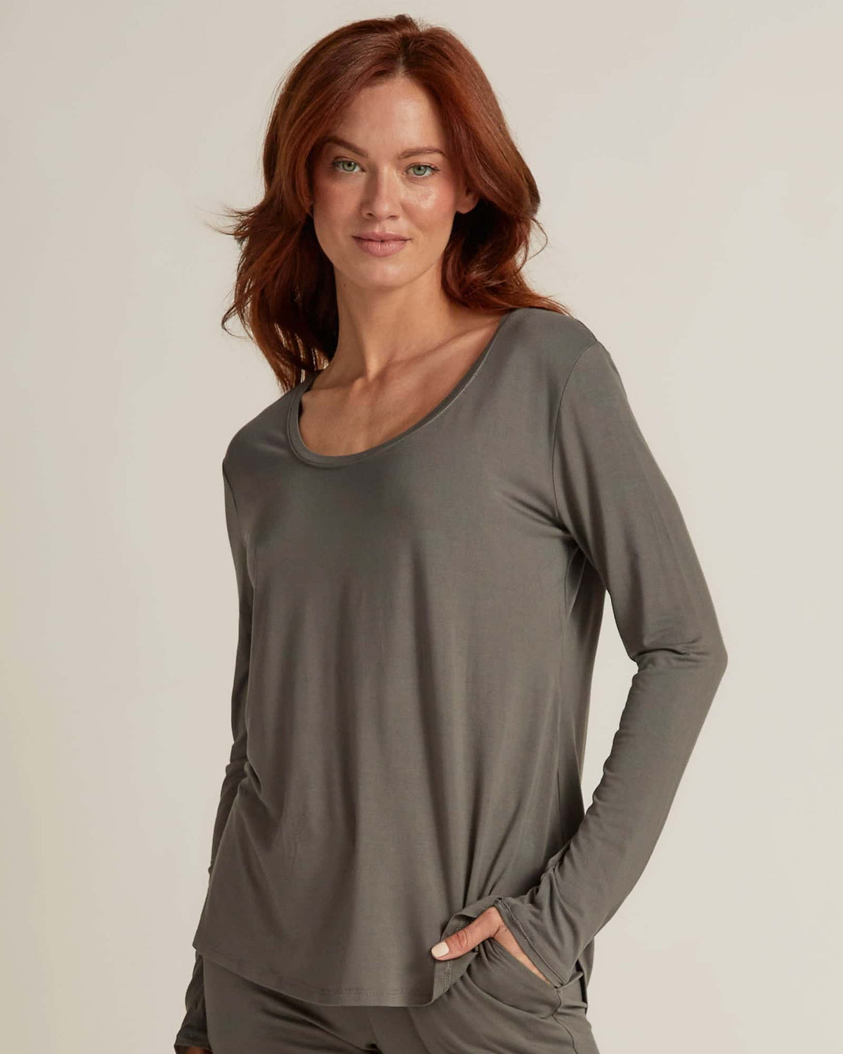 A woman wearing grey long sleeve top and matching pants, standing against a plain background