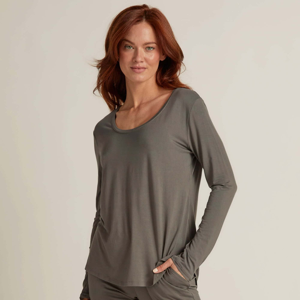 A woman wearing grey long sleeve top and matching pants, standing against a plain background