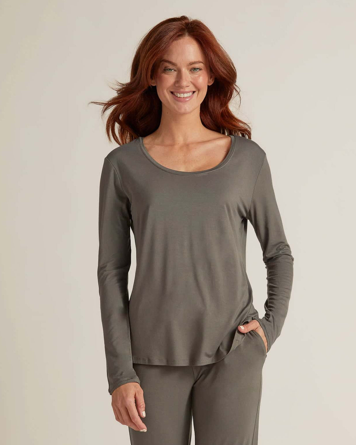 A woman wearing grey long sleeve top and matching pants, standing against a plain background
