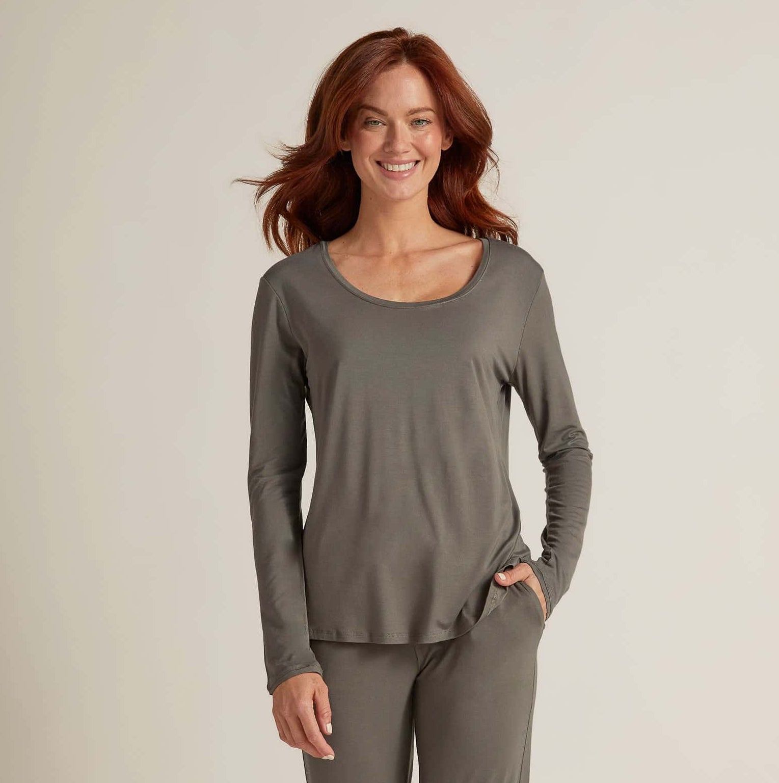 A woman wearing grey long sleeve top and matching pants, standing against a plain background