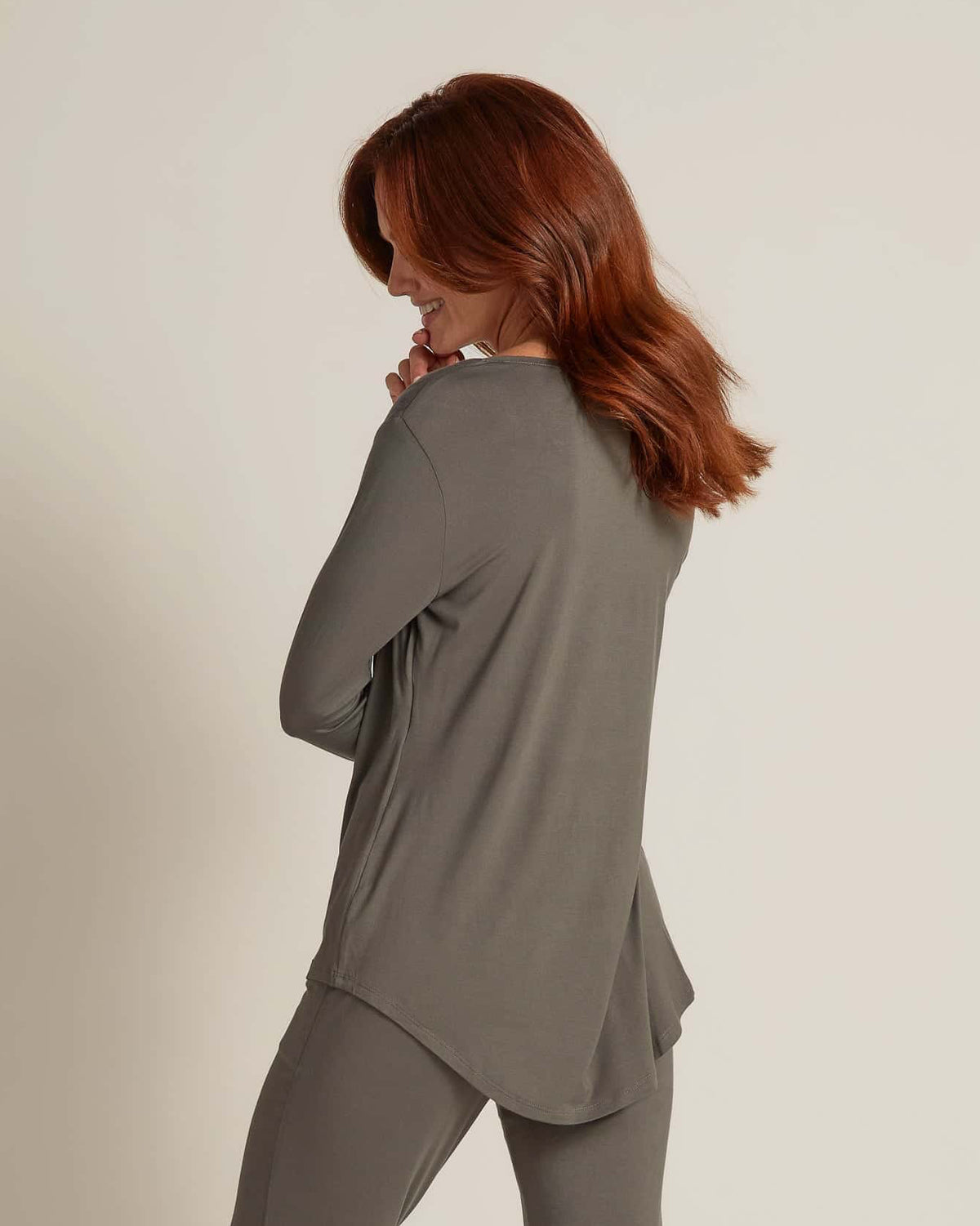 A woman wearing grey long sleeve top and matching pants, standing against a plain background