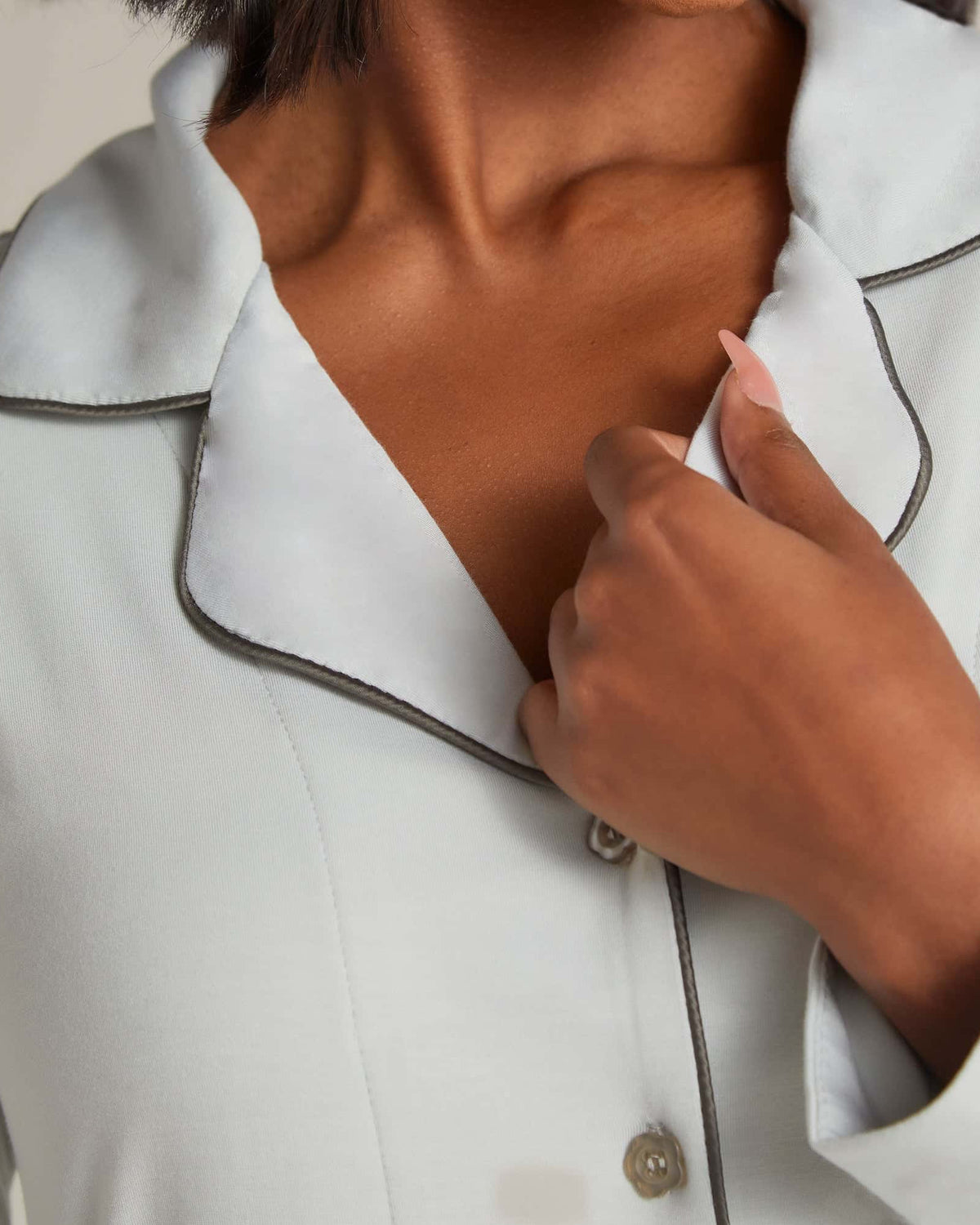 A woman standing and wearing a grey nightshirt with long sleeves and button-up front.