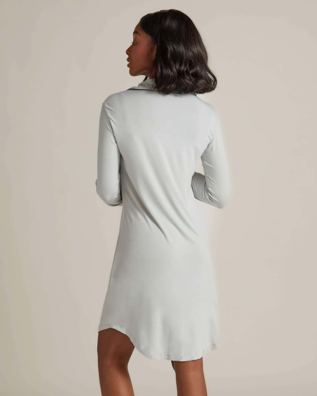 A woman standing and wearing a grey nightshirt with long sleeves and button-up front.