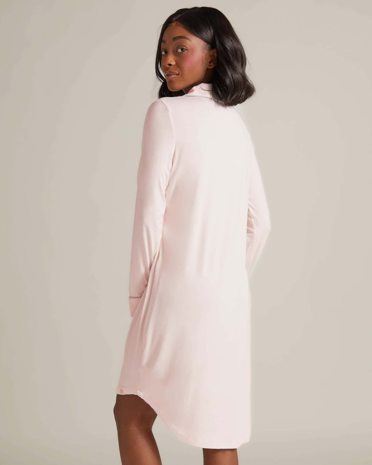 A woman standing and wearing a pink nightshirt with long sleeves and button-up front.