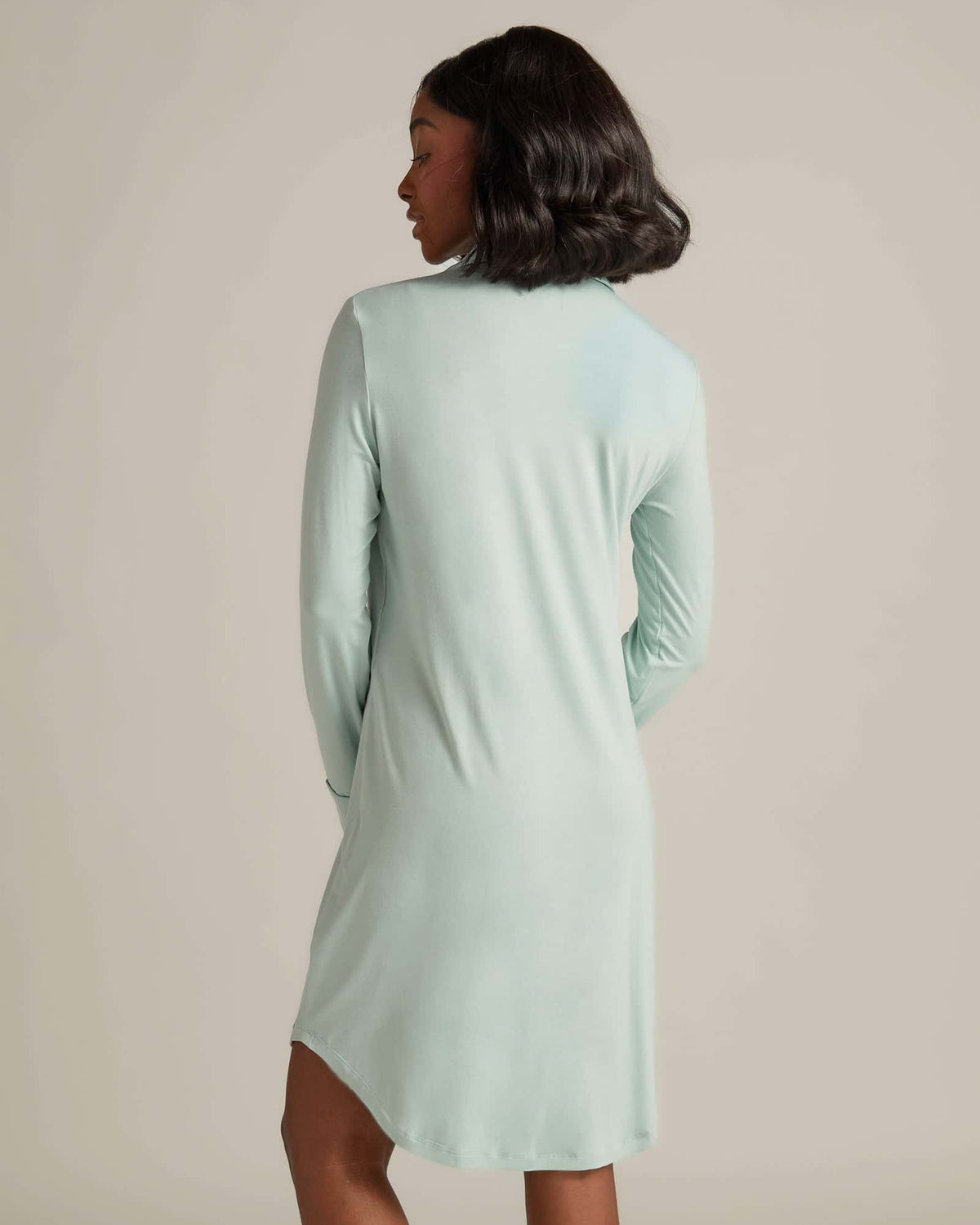 A woman standing and wearing an aqua nightshirt with long sleeves and button-up front.