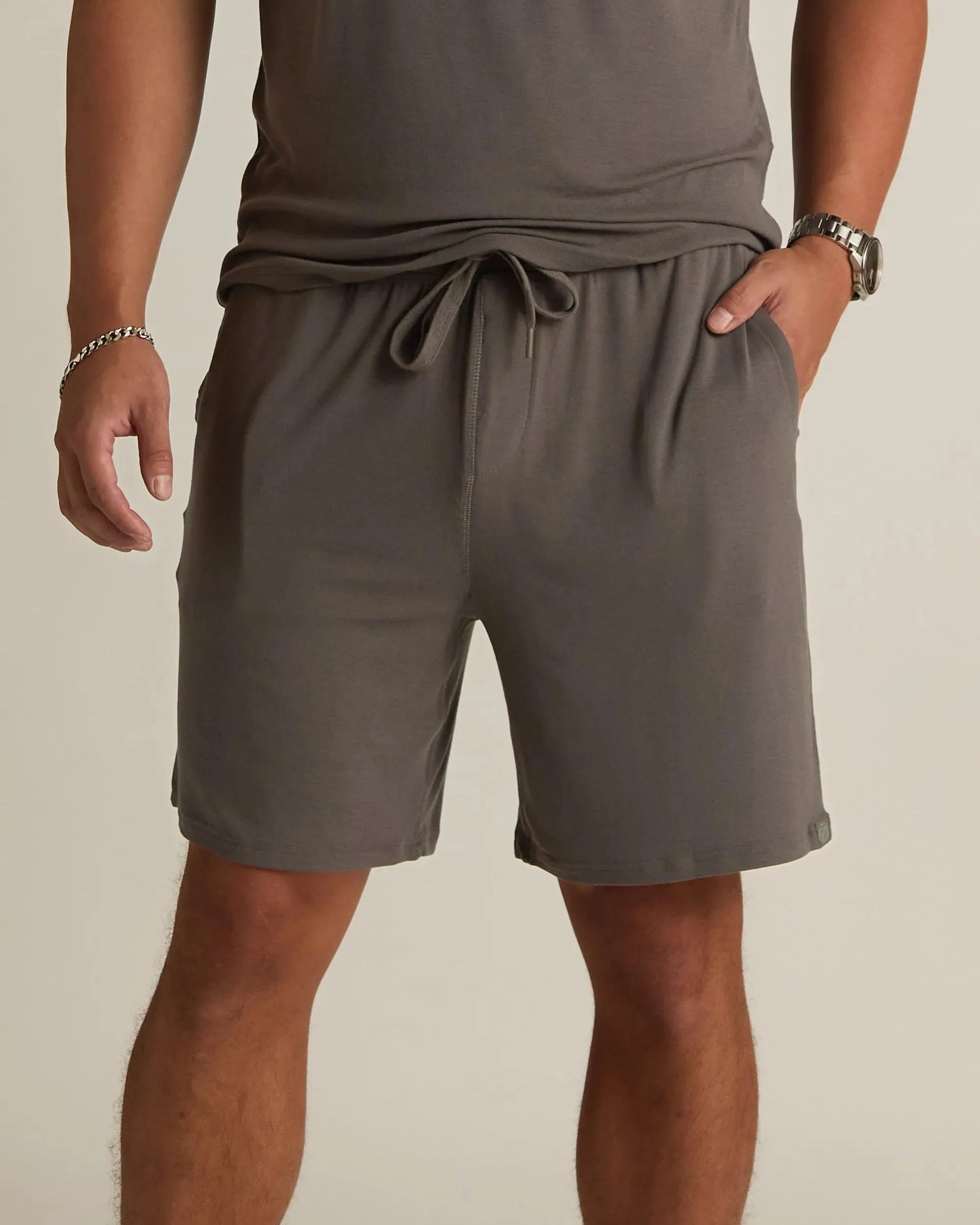 A man wearing gray lounge shorts with a drawstring waist, standing with one hand in a pocket.