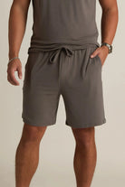A man wearing gray lounge shorts with a drawstring waist, standing with one hand in a pocket.