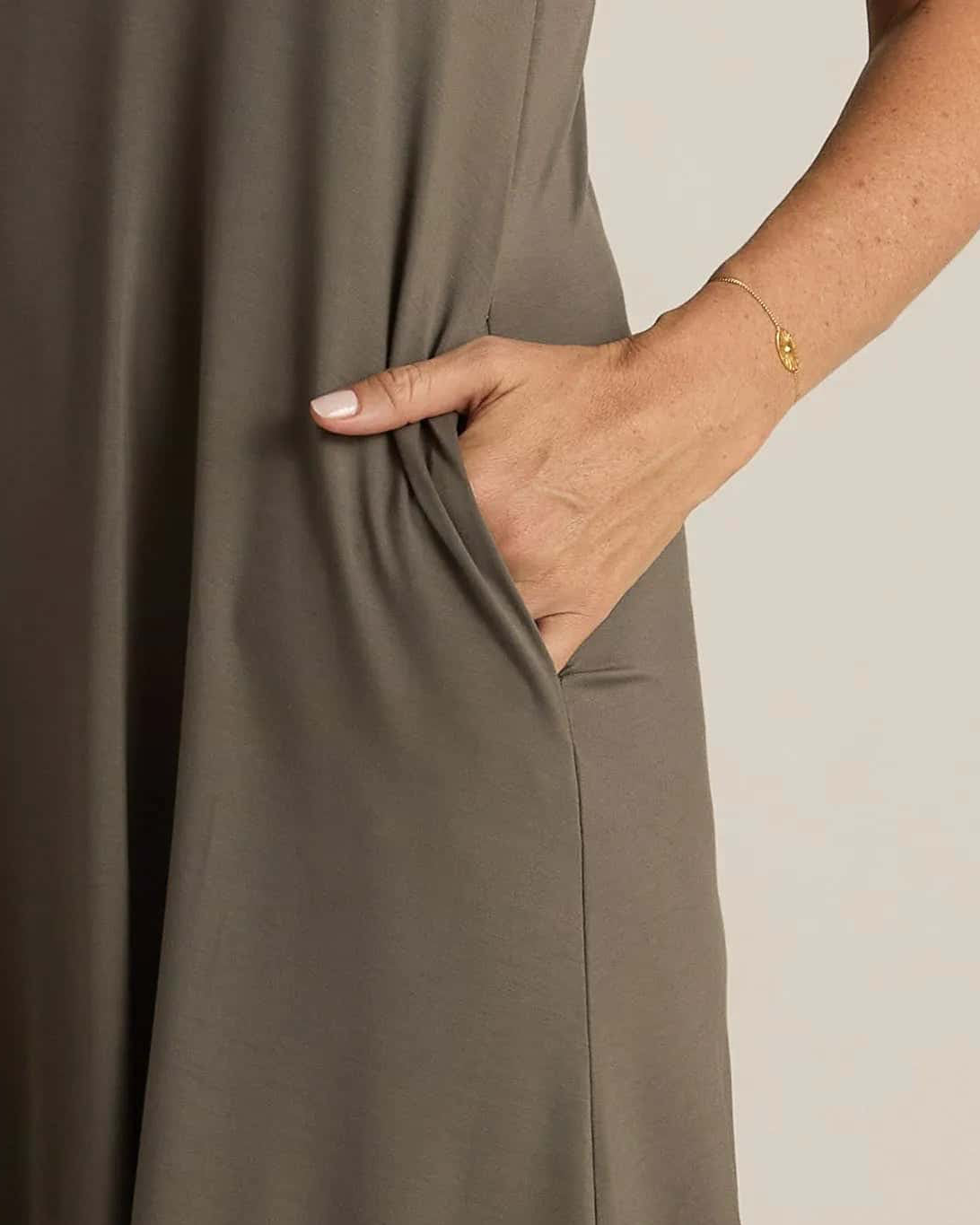 A woman standing, wearing a sleeveless grey nightshirt with a V-neckline in front and back, side pockets, and an A-line hem.