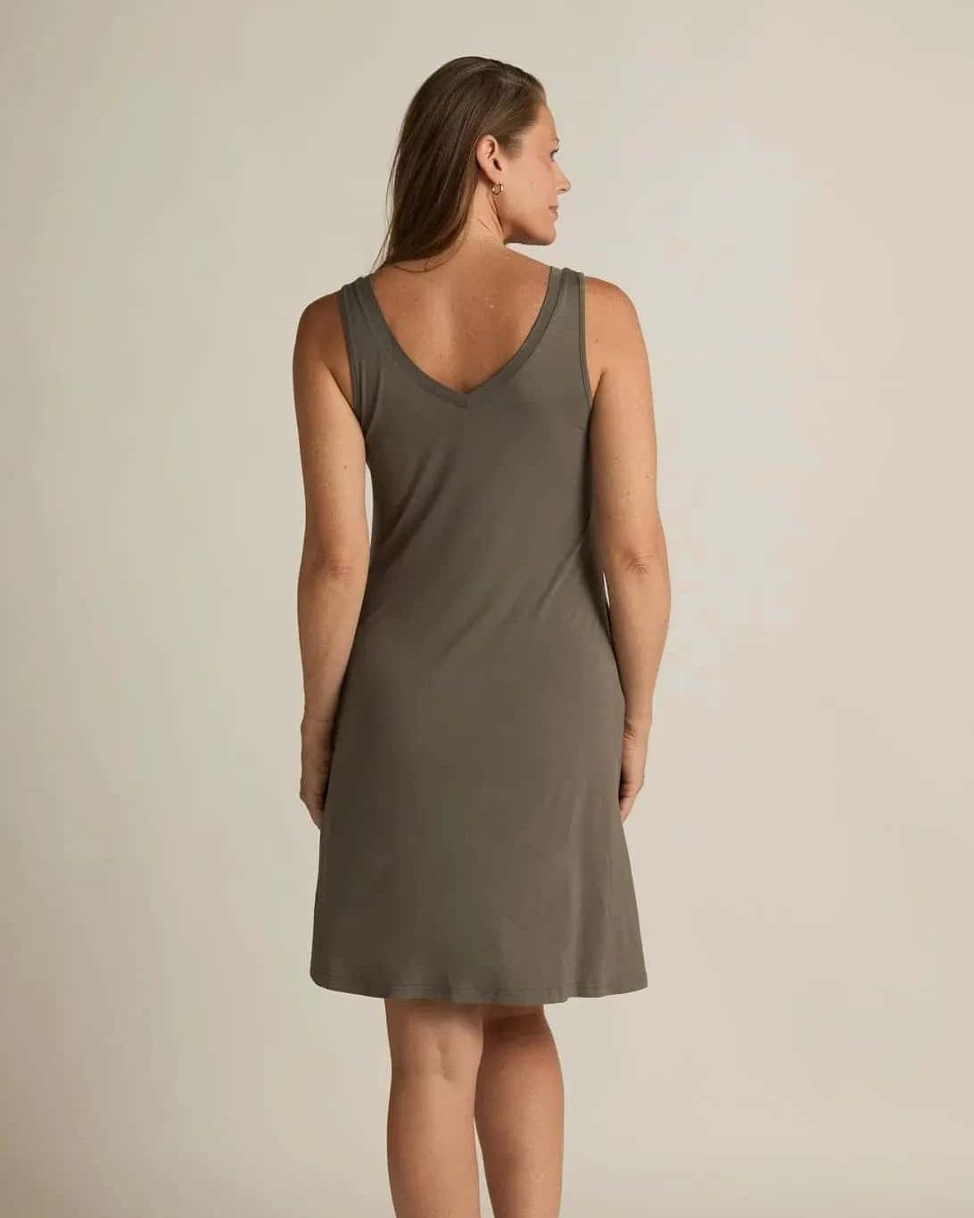 A woman standing, wearing a sleeveless grey nightshirt with a V-neckline in front and back, side pockets, and an A-line hem.
