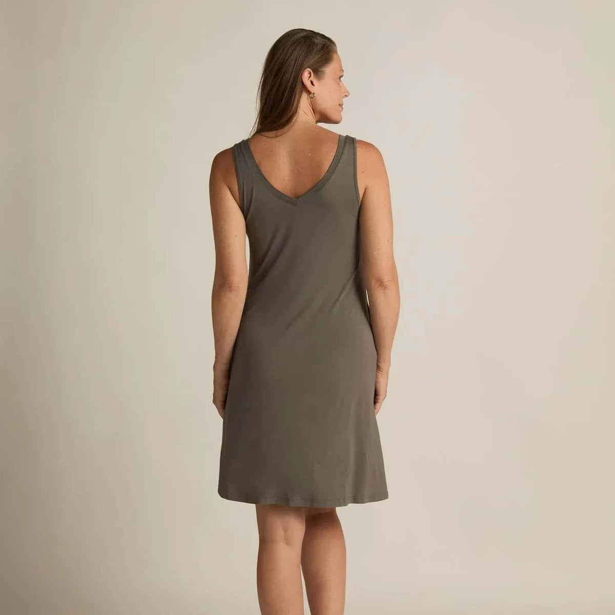 A woman standing, wearing a sleeveless grey nightshirt with a V-neckline in front and back, side pockets, and an A-line hem.