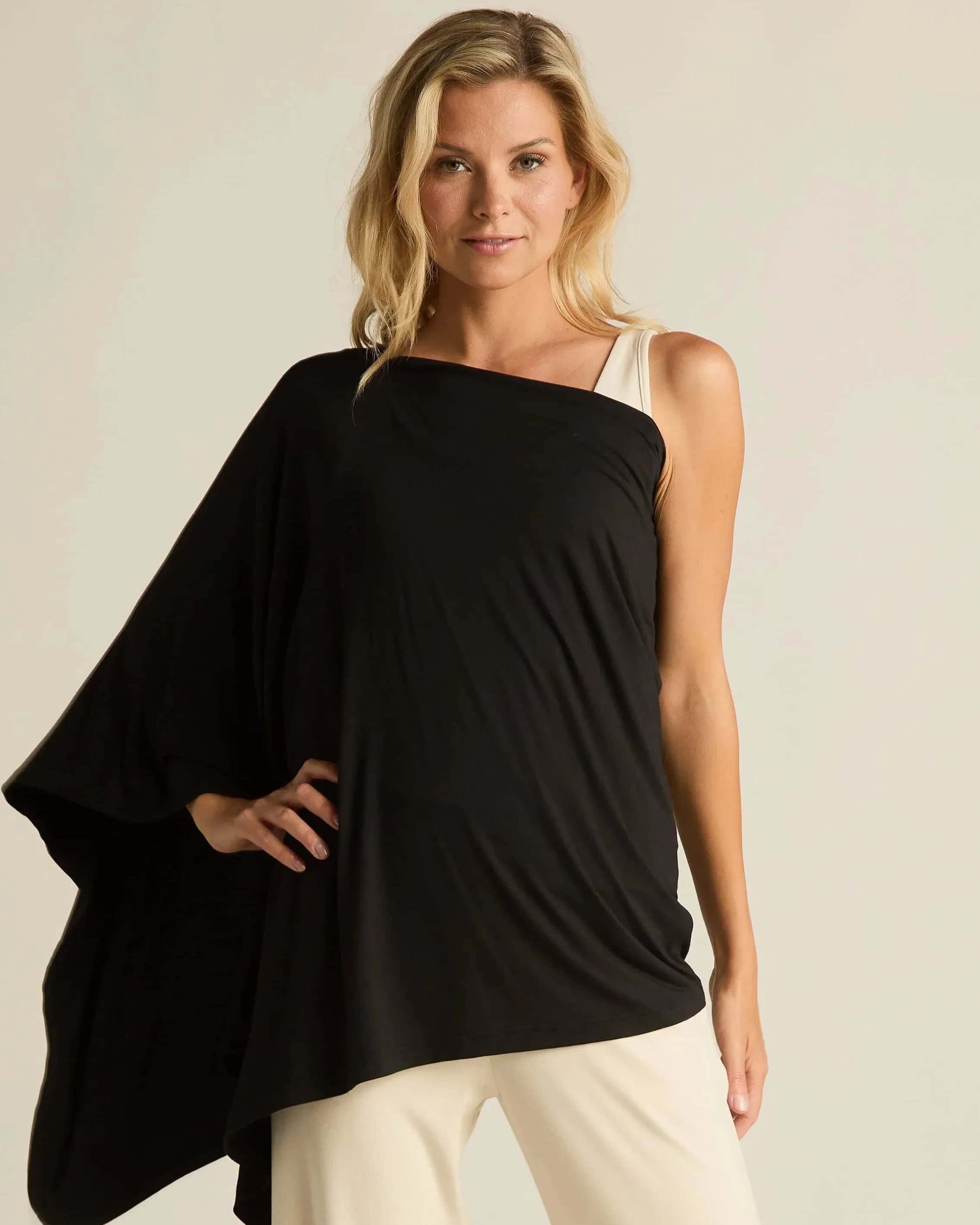 Woman wearing a black one-shoulder top and beige pants against a plain background