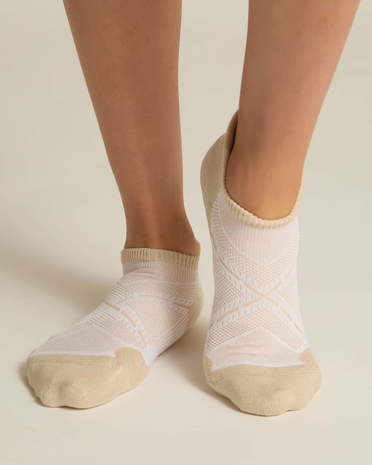 A pair of beige ankle socks with padding at the toe and heel areas, displayed on a person's feet against a white background.