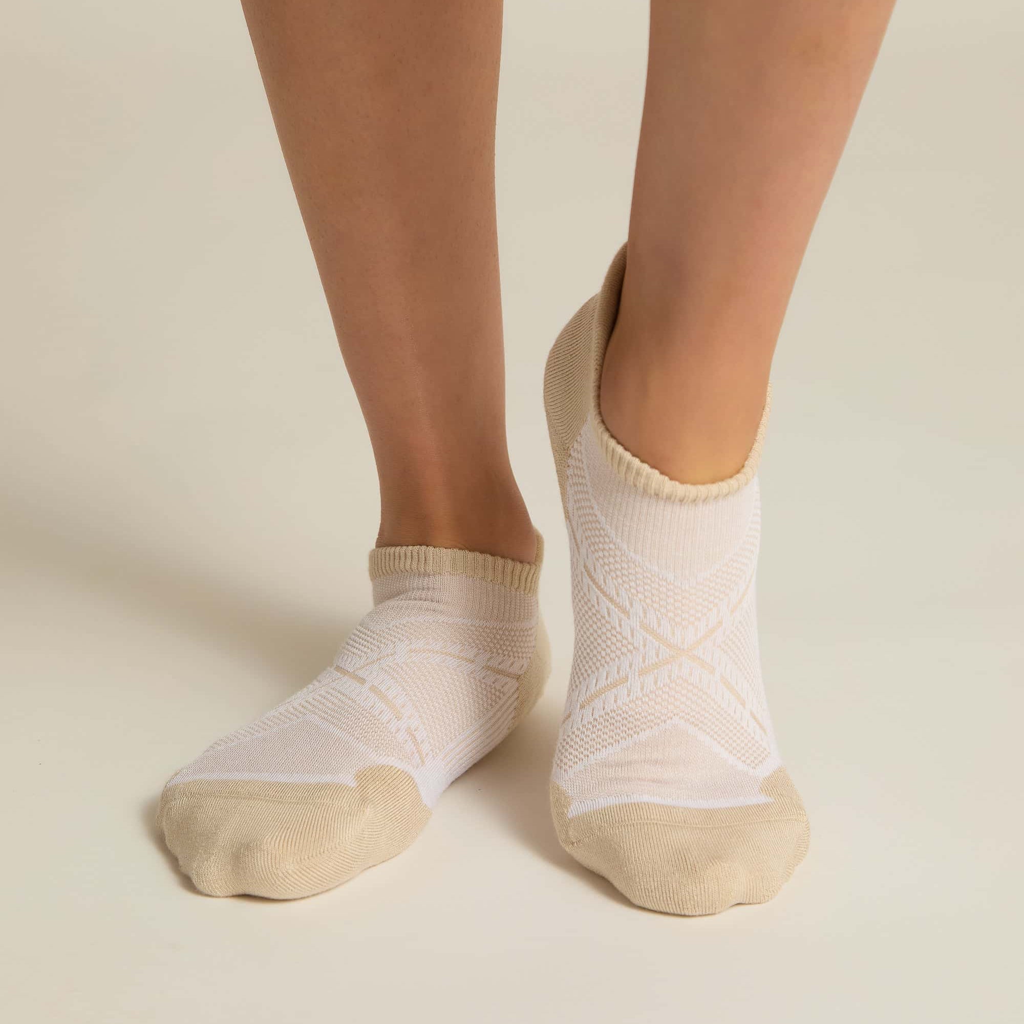 A pair of beige ankle socks with padding at the toe and heel areas, displayed on a person's feet against a white background.