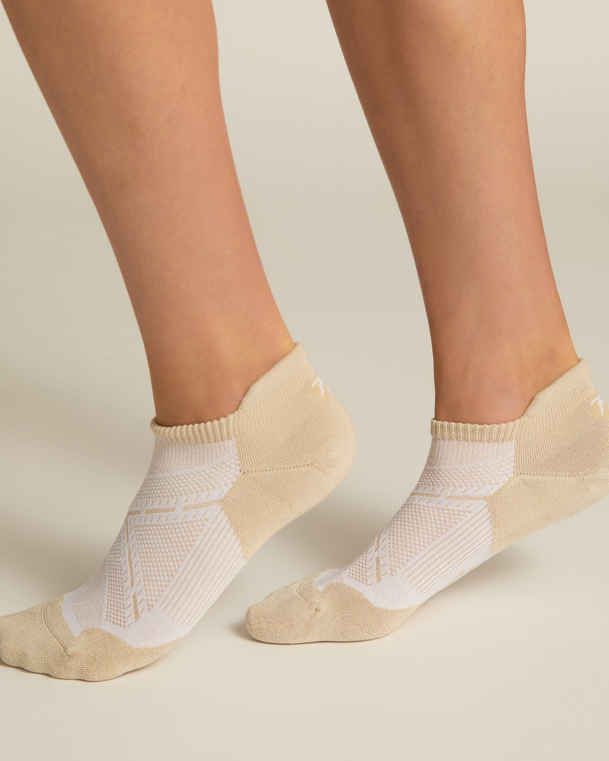 A pair of beige ankle socks with padding at the toe and heel areas, displayed on a person's feet against a white background.
