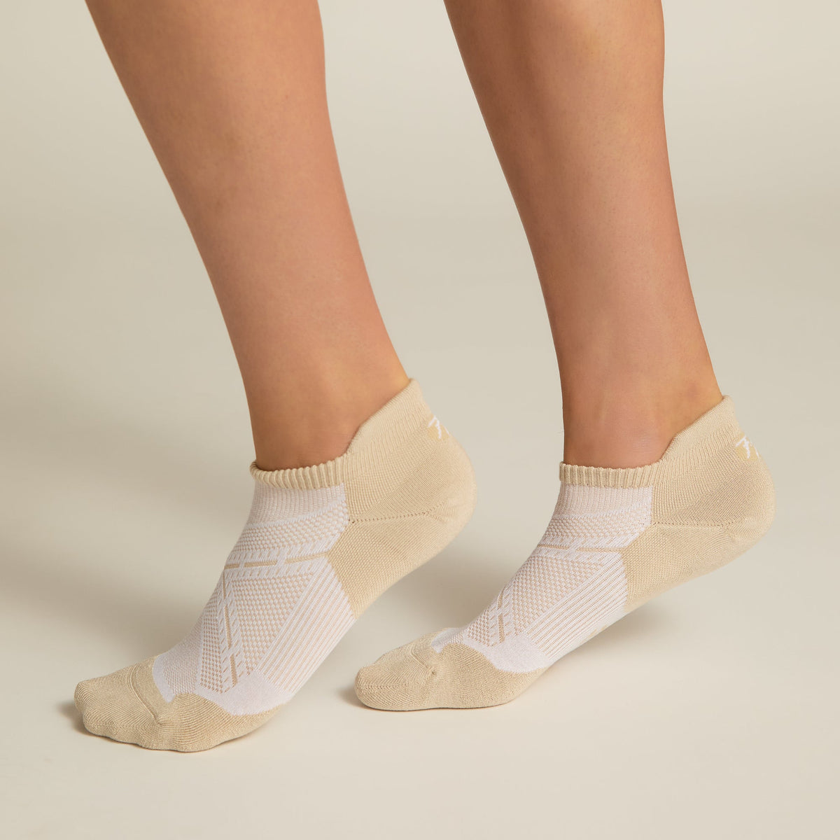 A pair of beige ankle socks with padding at the toe and heel areas, displayed on a person's feet against a white background.