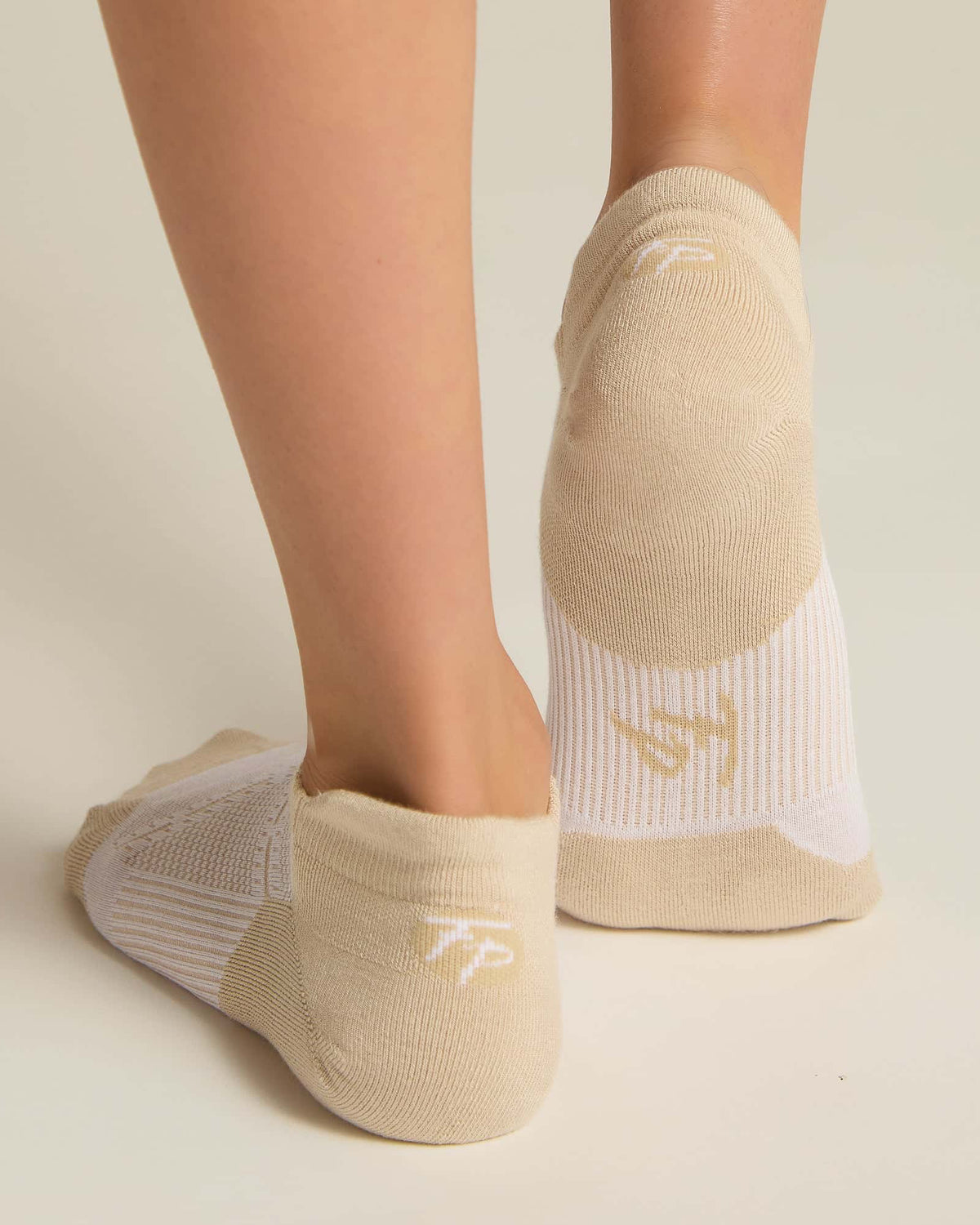 A pair of beige ankle socks with padding at the toe and heel areas, displayed on a person's feet against a white background.