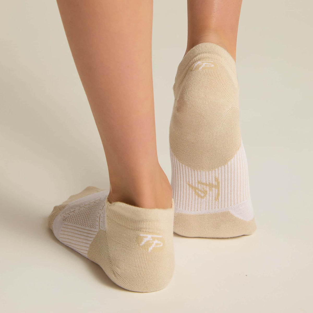 A pair of beige ankle socks with padding at the toe and heel areas, displayed on a person's feet against a white background.