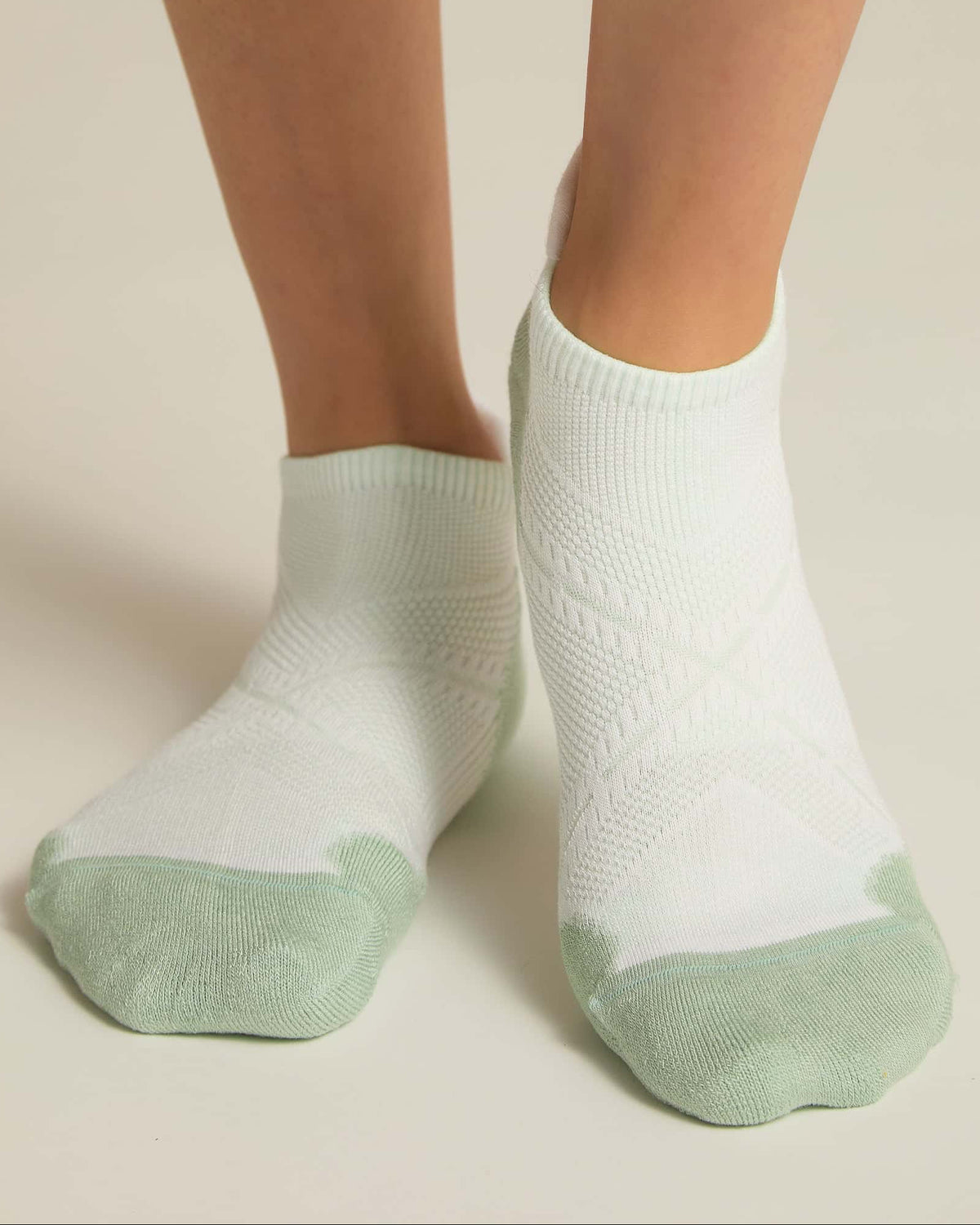 A pair of white and aqua ankle socks with padding at the toe and heel areas, displayed on a person's feet against a white background.