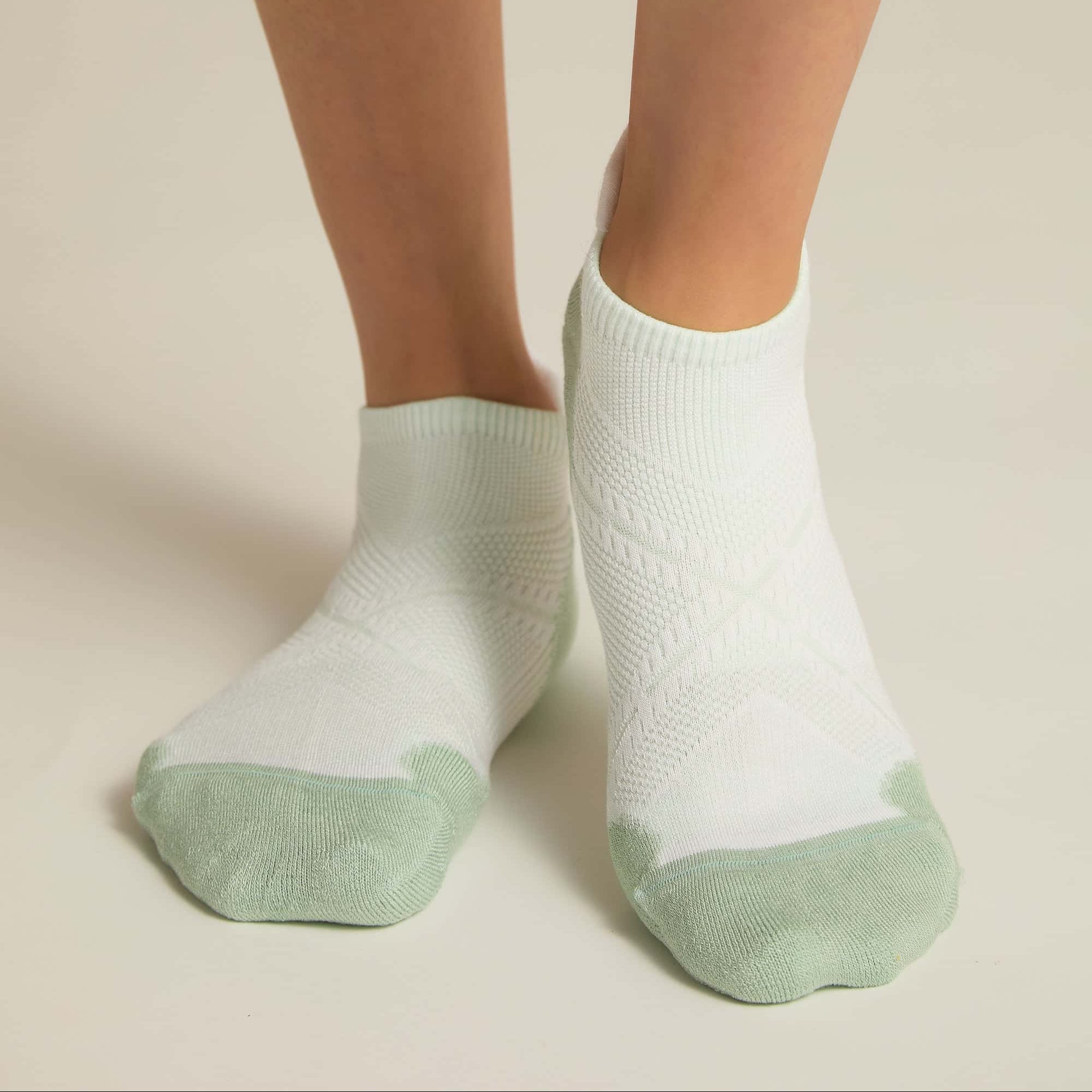 A pair of white and aqua ankle socks with padding at the toe and heel areas, displayed on a person's feet against a white background.