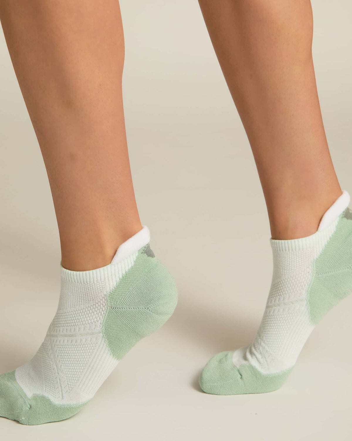 A pair of white and aqua ankle socks with padding at the toe and heel areas, displayed on a person's feet against a white background.