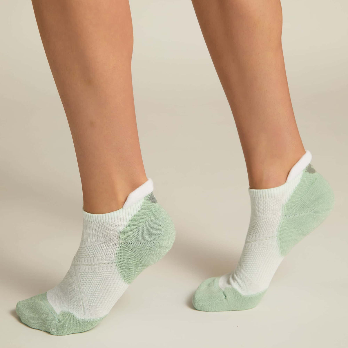 A pair of white and aqua ankle socks with padding at the toe and heel areas, displayed on a person's feet against a white background.