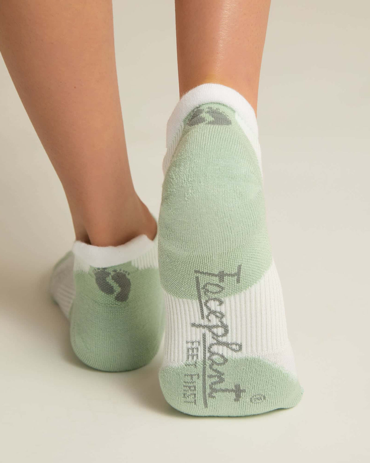 A pair of white and aqua ankle socks with padding at the toe and heel areas, displayed on a person's feet against a white background.