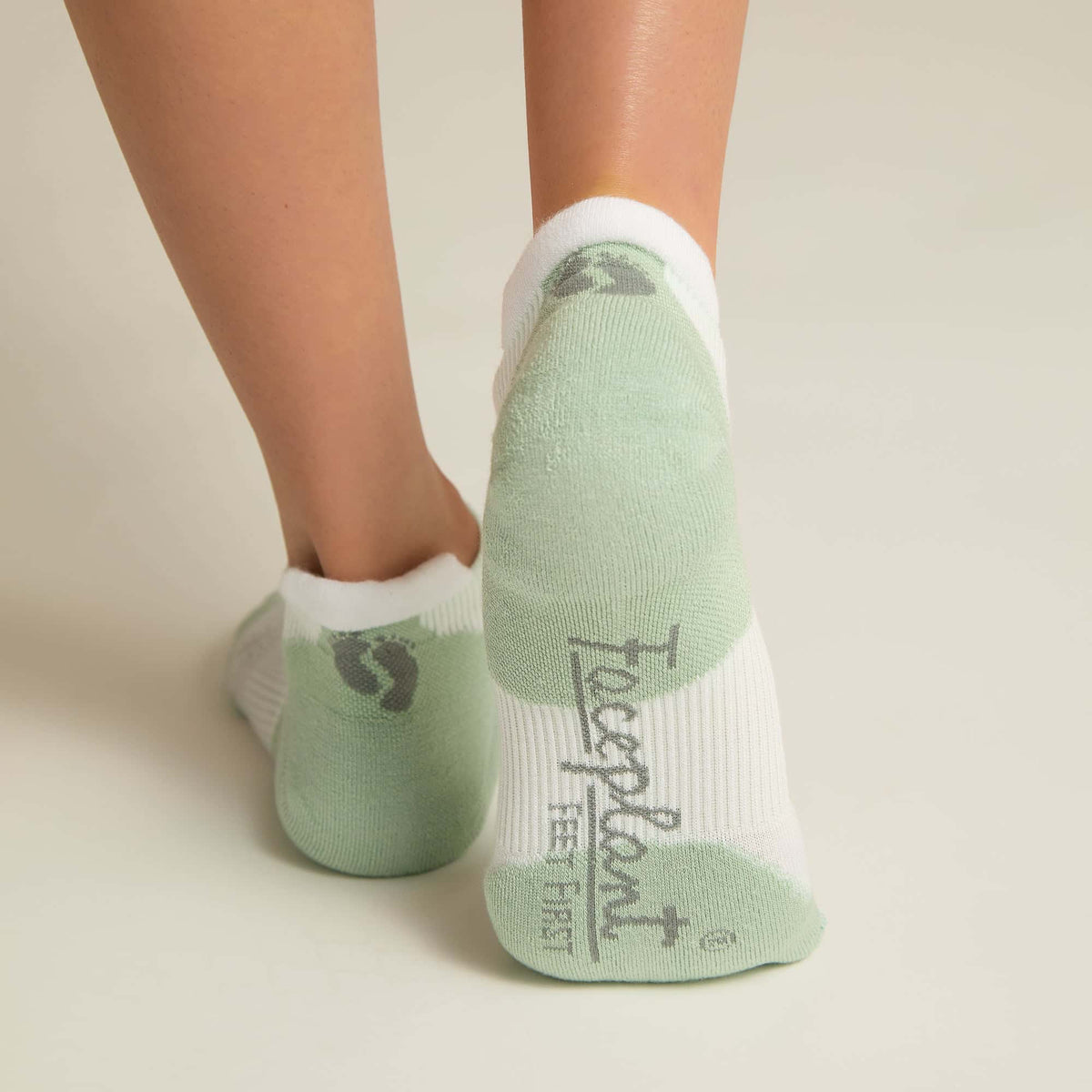 A pair of white and aqua ankle socks with padding at the toe and heel areas, displayed on a person's feet against a white background.