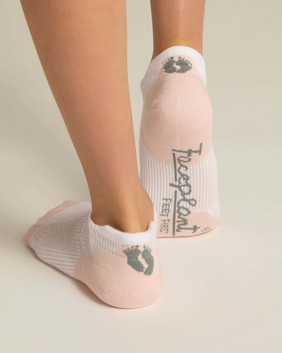 A pair of pink ankle socks with padding at the toe and heel areas, displayed on a person's feet against a white background.