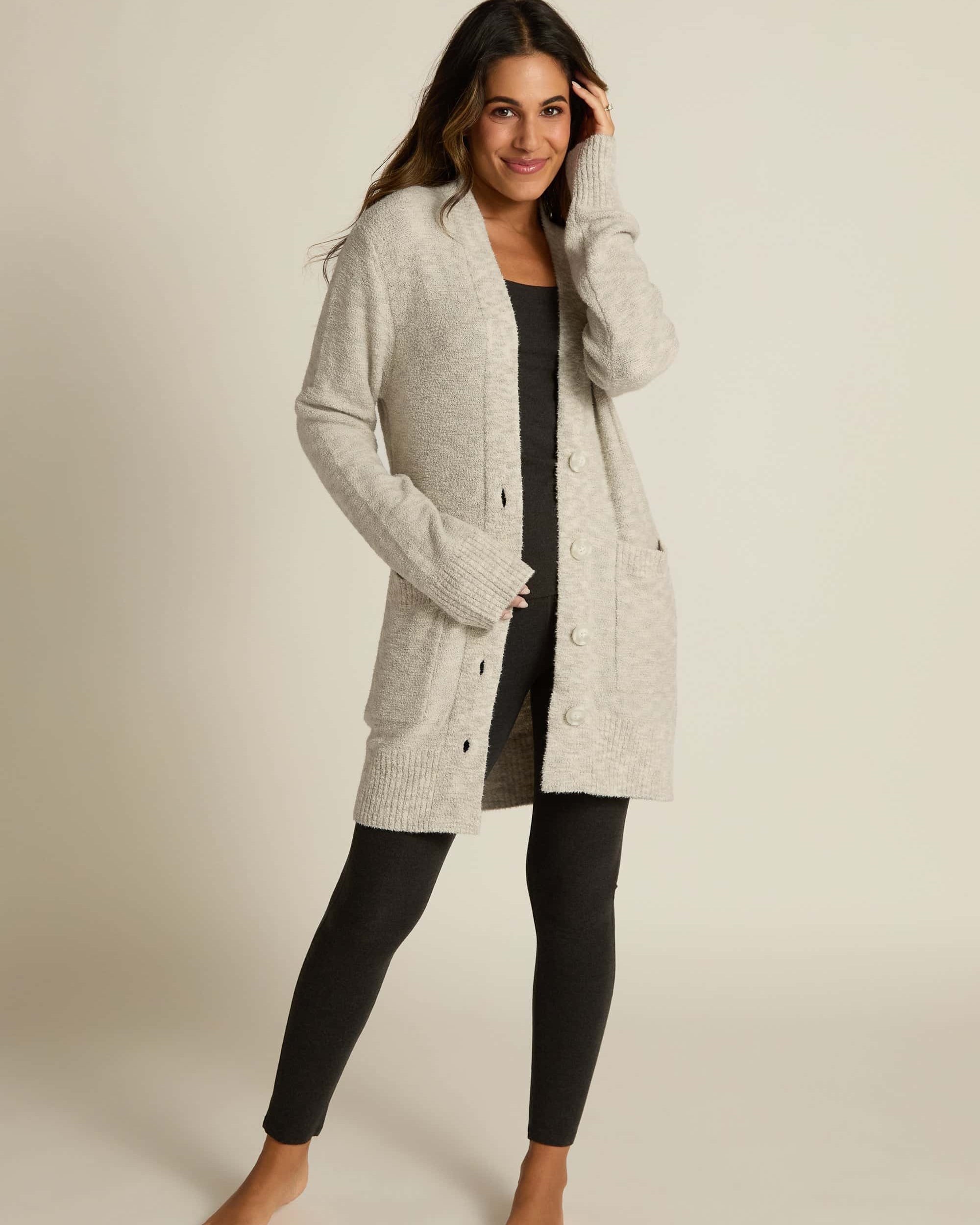 A female model wearing a gray button-up cardigan with side pockets over a matching black shirt and leggings.