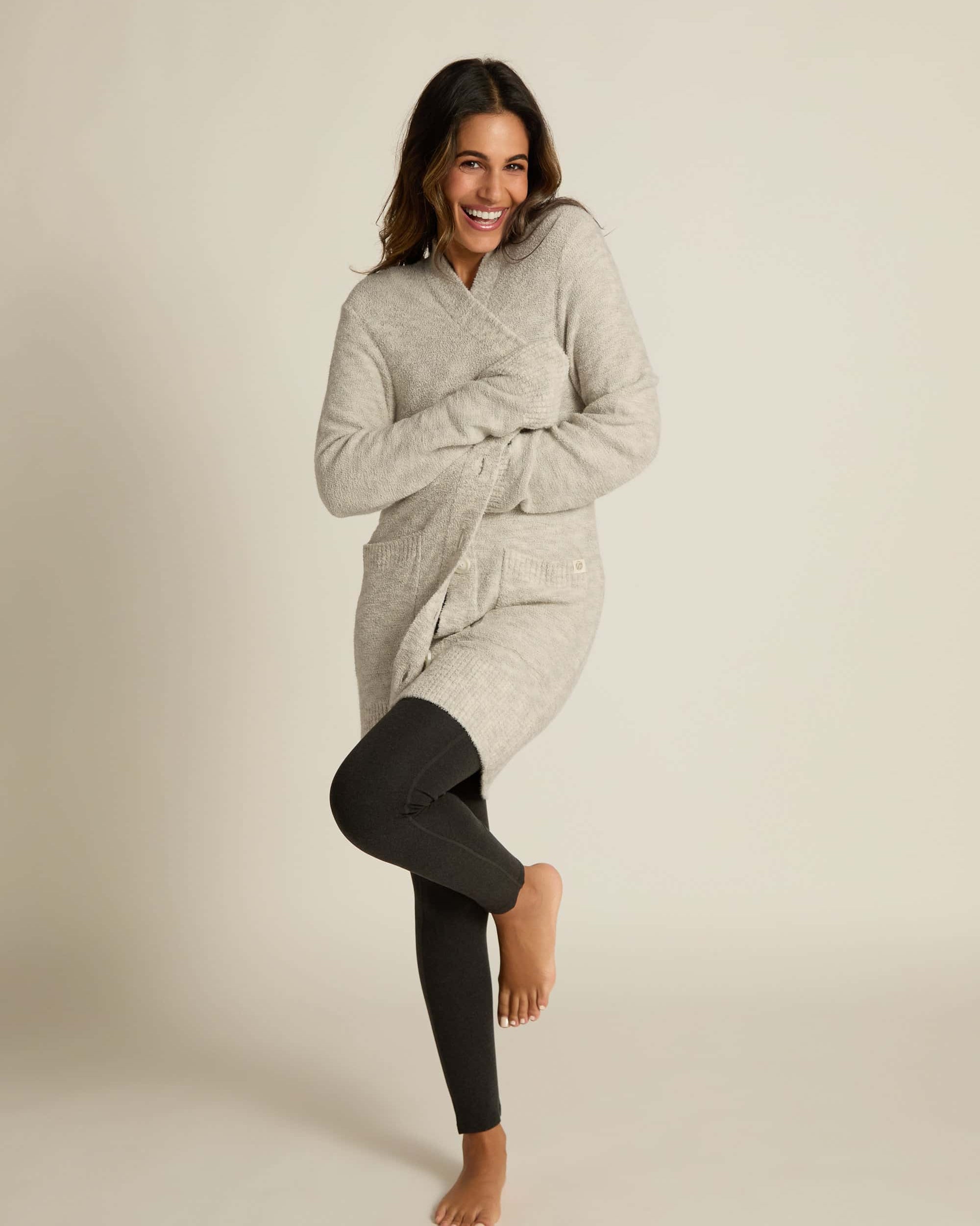 A female model wraping up in a gray button-up cardigan with side pockets over a matching black shirt and leggings.