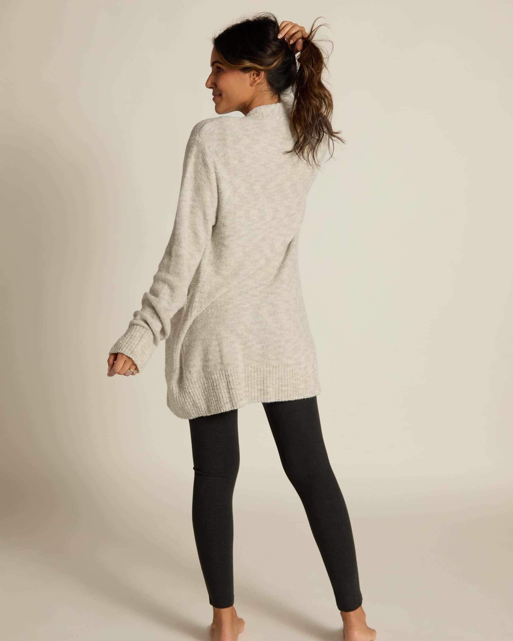A female model wearing a gray button-up cardigan with side pockets overblack leggings.