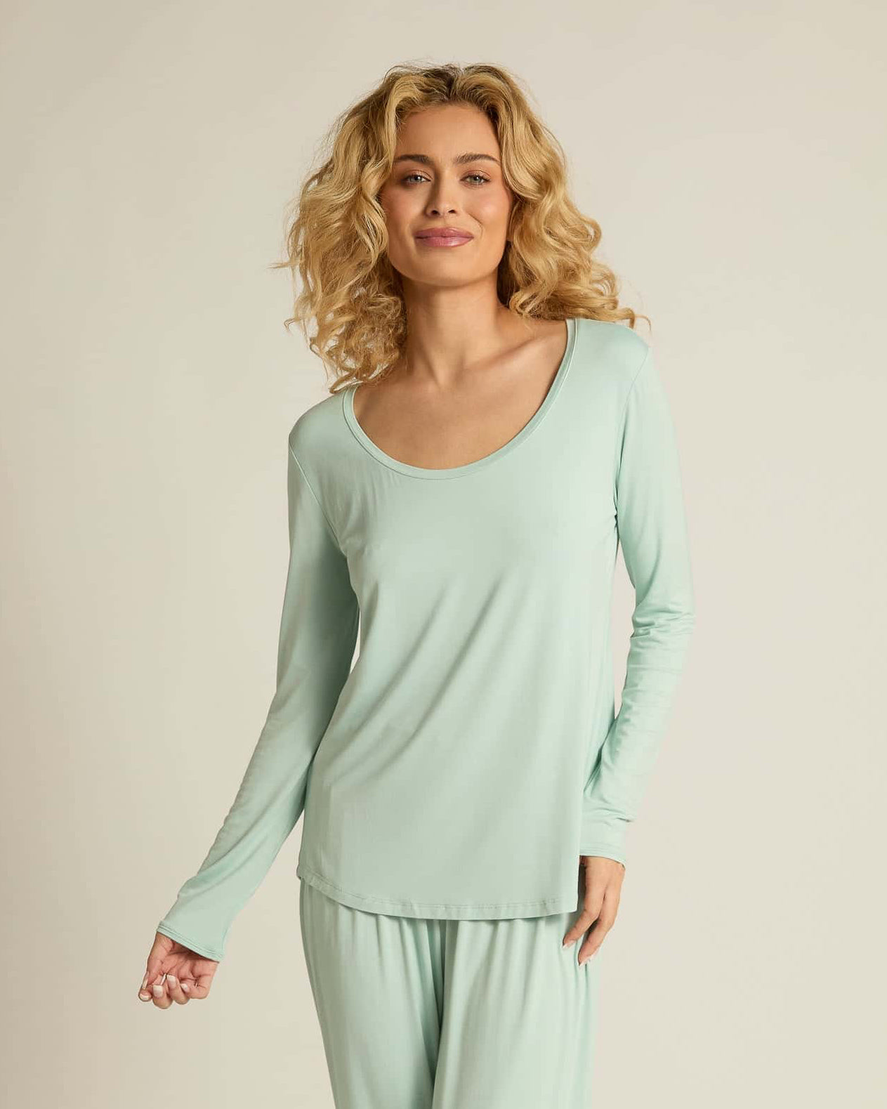 A woman wearing aqua long sleeve top and matching pants, standing against a plain background