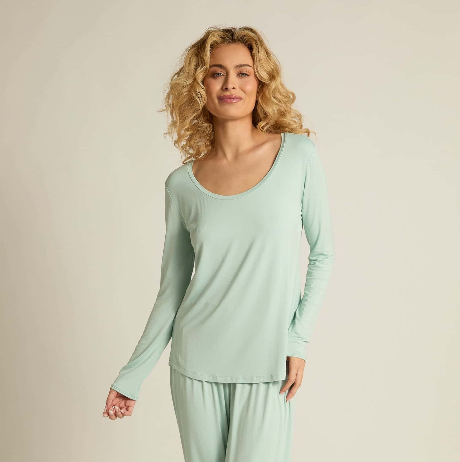 A woman wearing aqua long sleeve top and matching pants, standing against a plain background